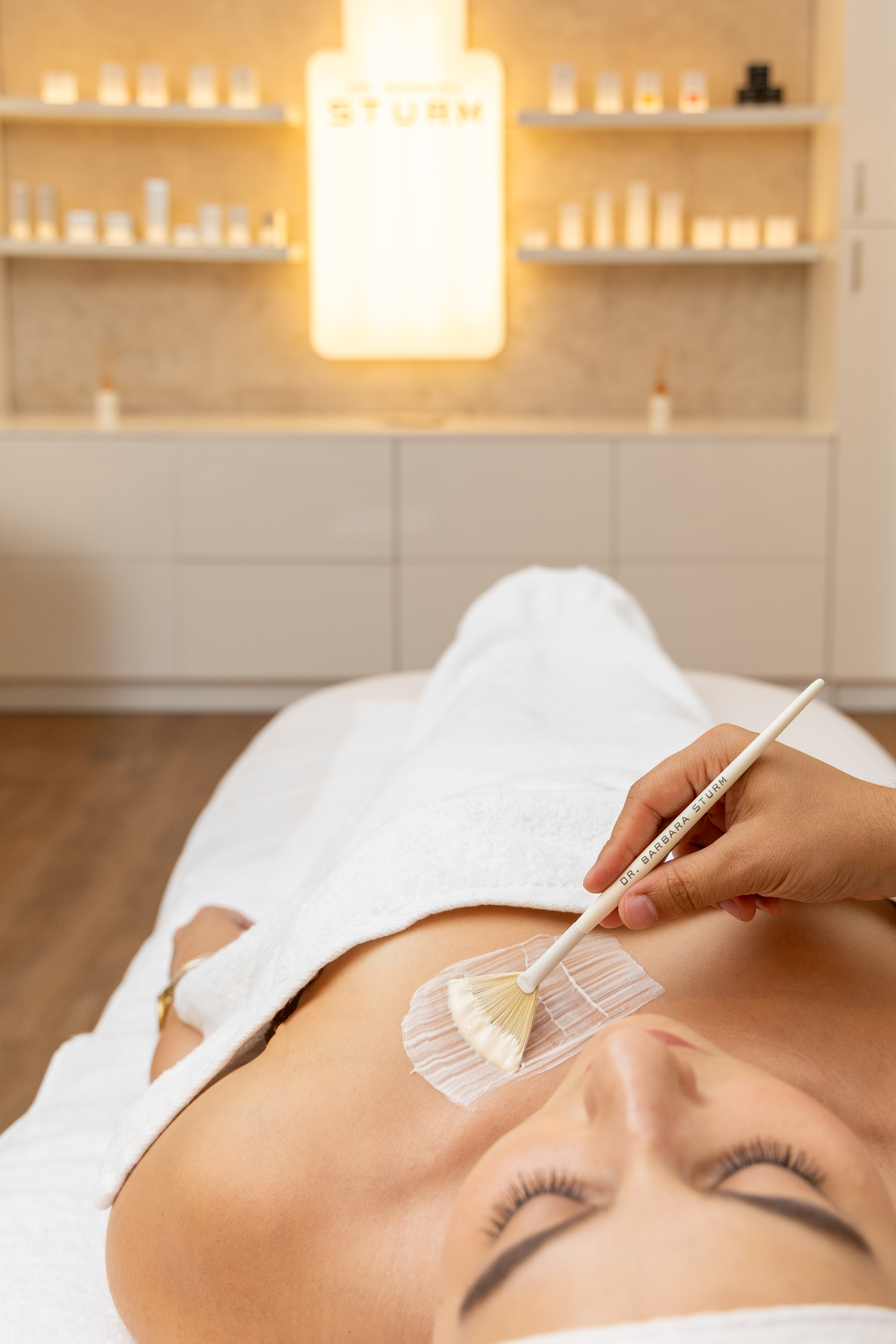 Therapist applying premium body treatment product with a brush to a woman's chest in a serene treatment room