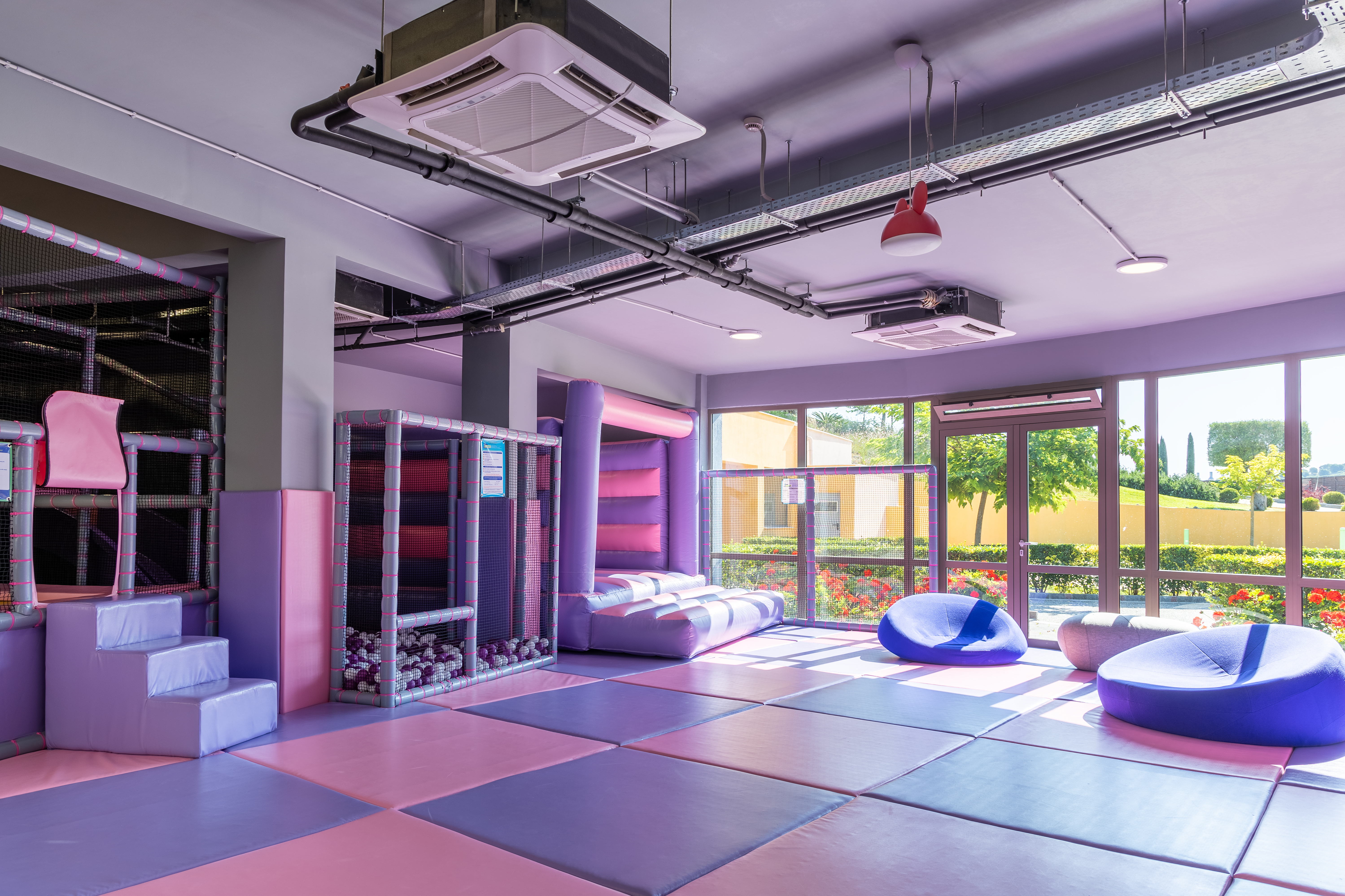 Bright indoor soft play area with padded floors, ball pit, and lounge seating