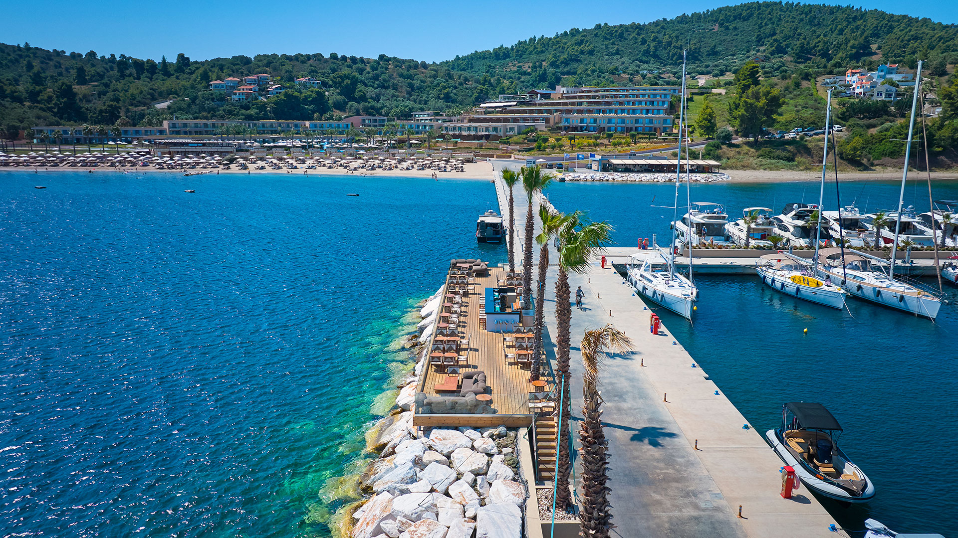 Side aerial view of Mirage On The Rocks bar with marina dock, beach, and resort in the background