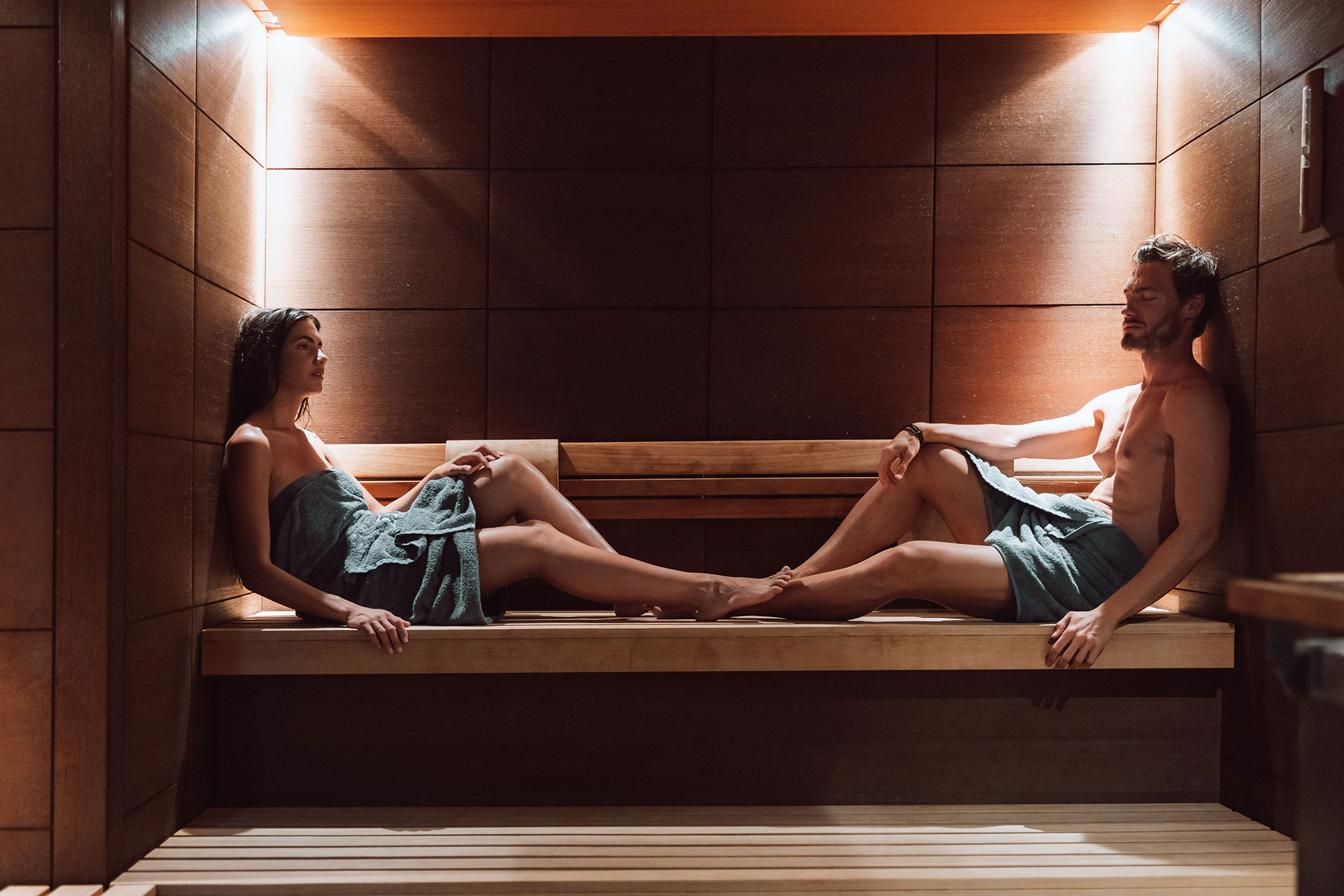 Couple relaxing in a wooden sauna under soft warm lighting