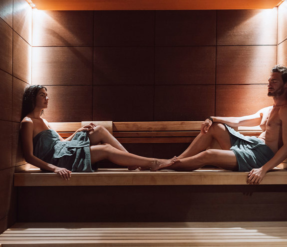 Couple relaxing in a wooden sauna under soft warm lighting