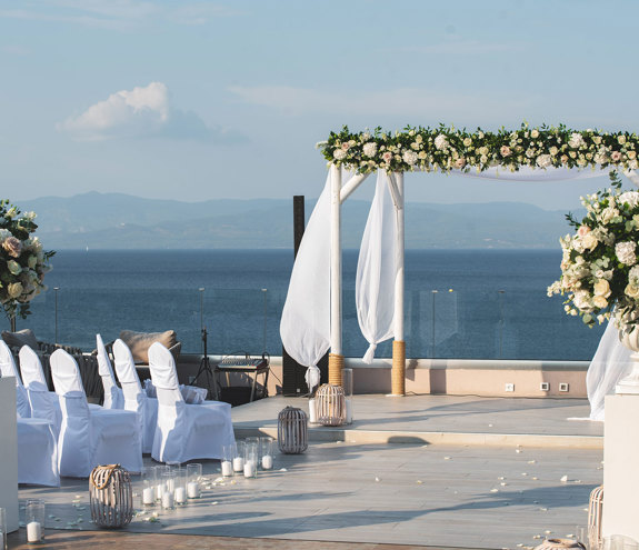 Seaside wedding ceremony setup with floral arch, white chairs and elegant decor