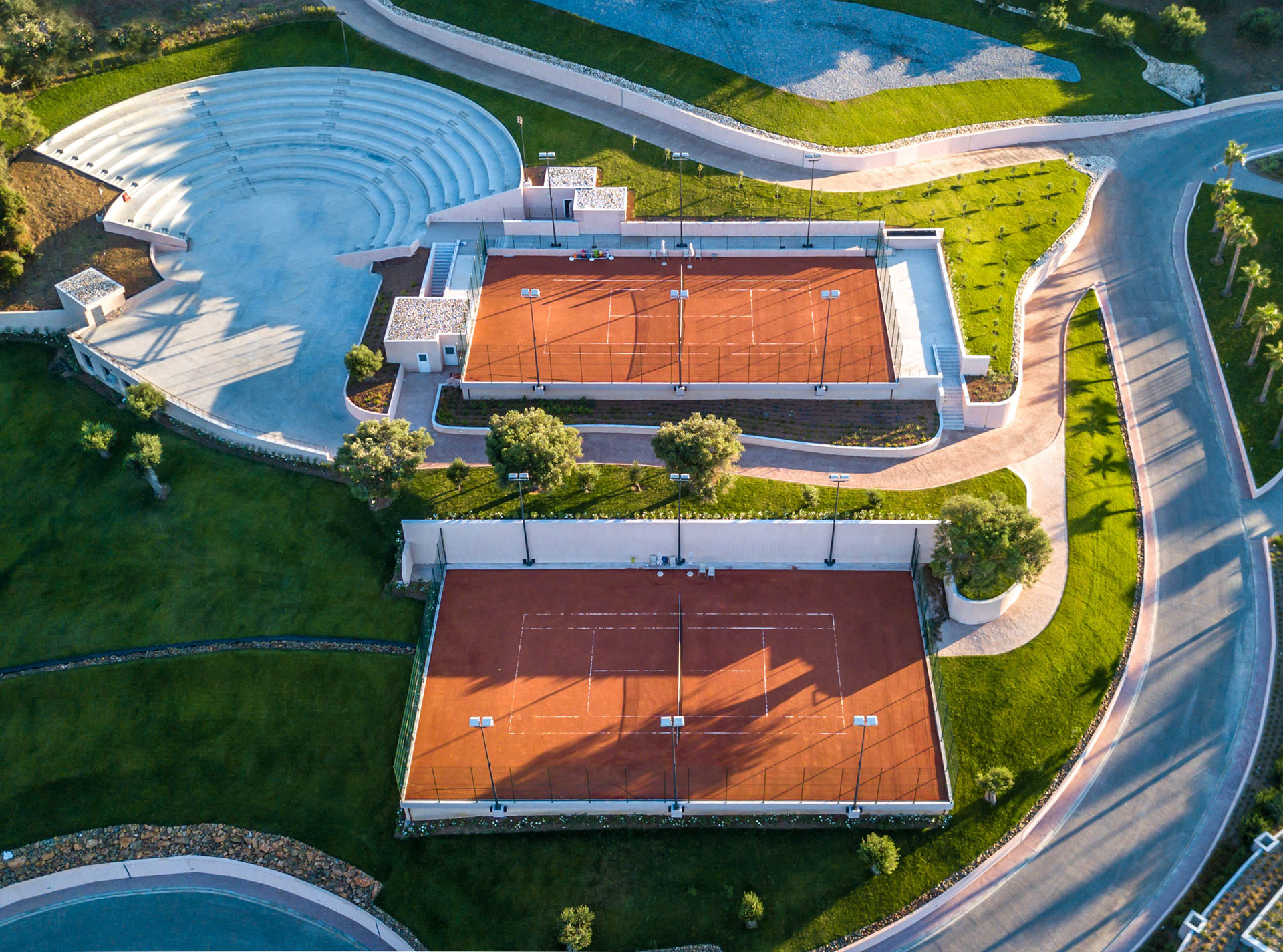 Aerial view of outdoor clay tennis courts and amphitheater surrounded by greenery