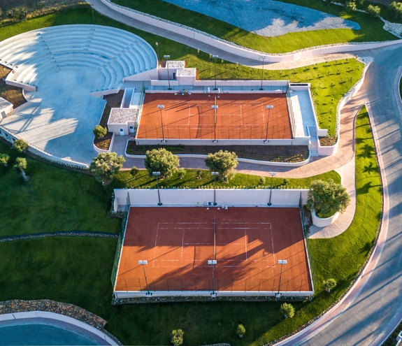 Aerial view of outdoor clay tennis courts and amphitheater surrounded by greenery