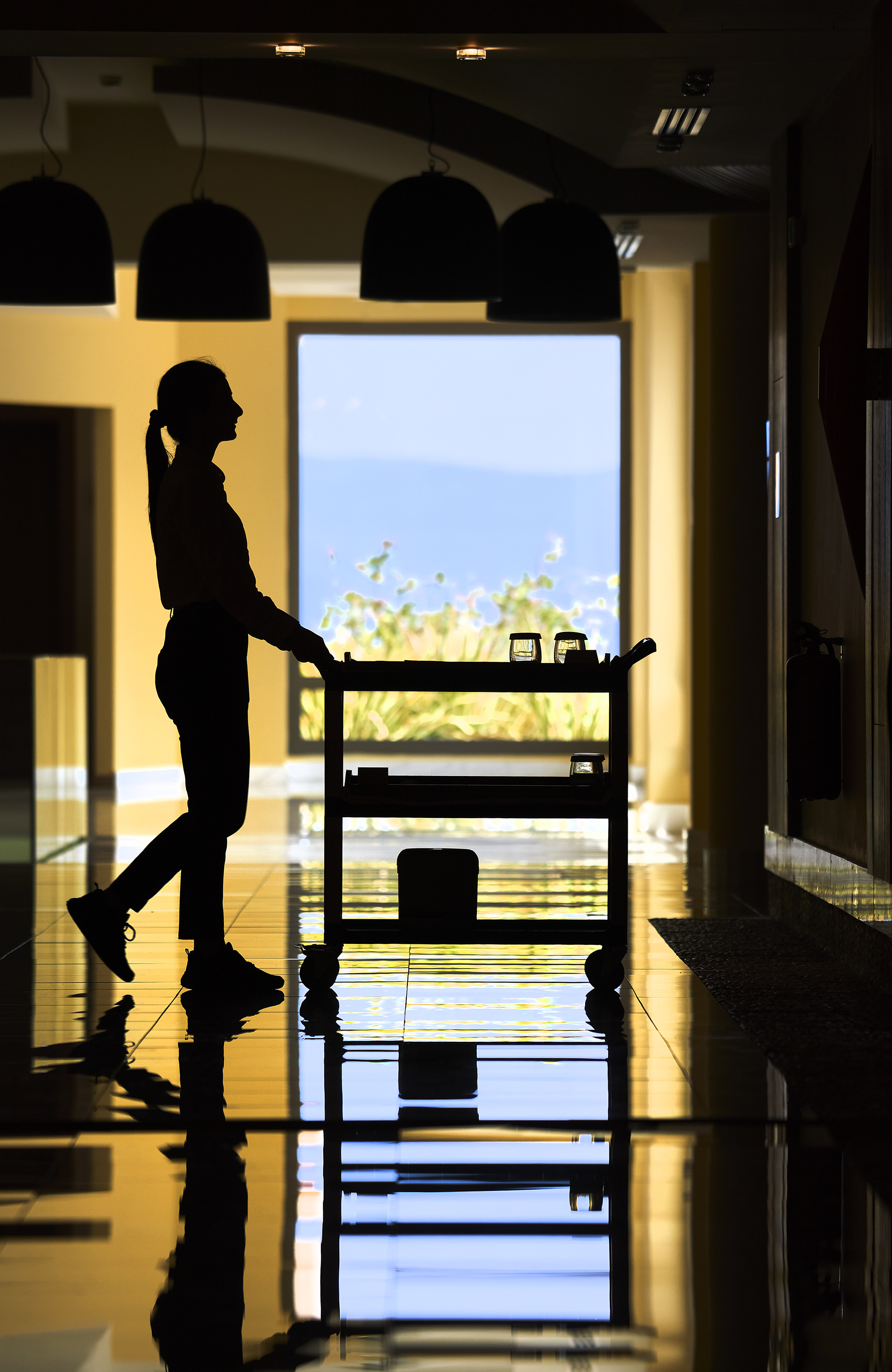 Hotel staff member with service cart walking through a sunlit corridor with ocean view