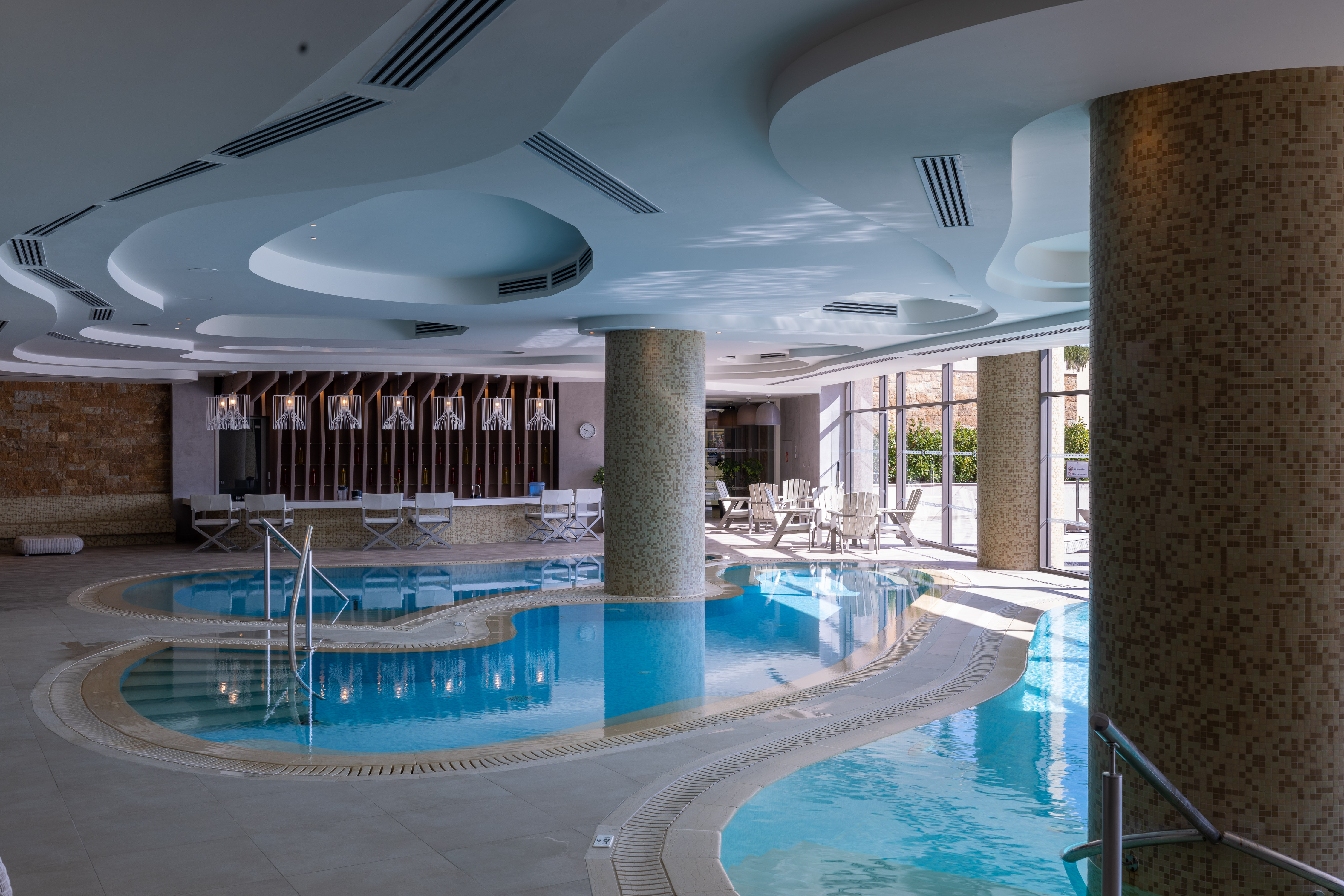 Luxury indoor pool with curved architecture, natural light and seating area