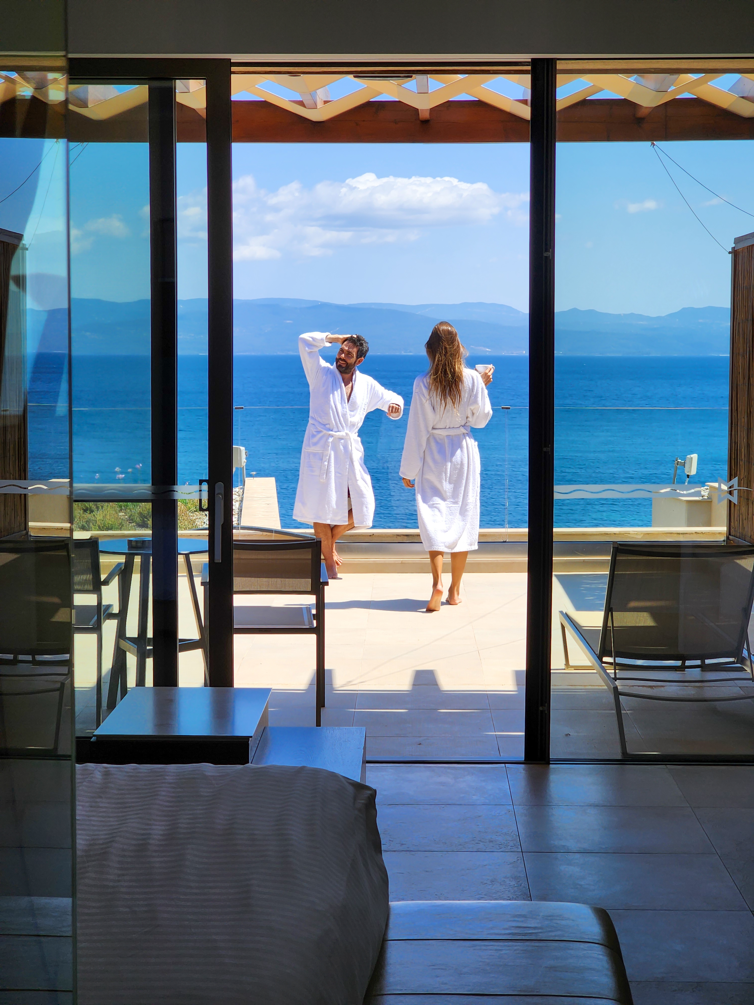 Couple in bathrobes enjoying sea view from private terrace suite with infinity pool