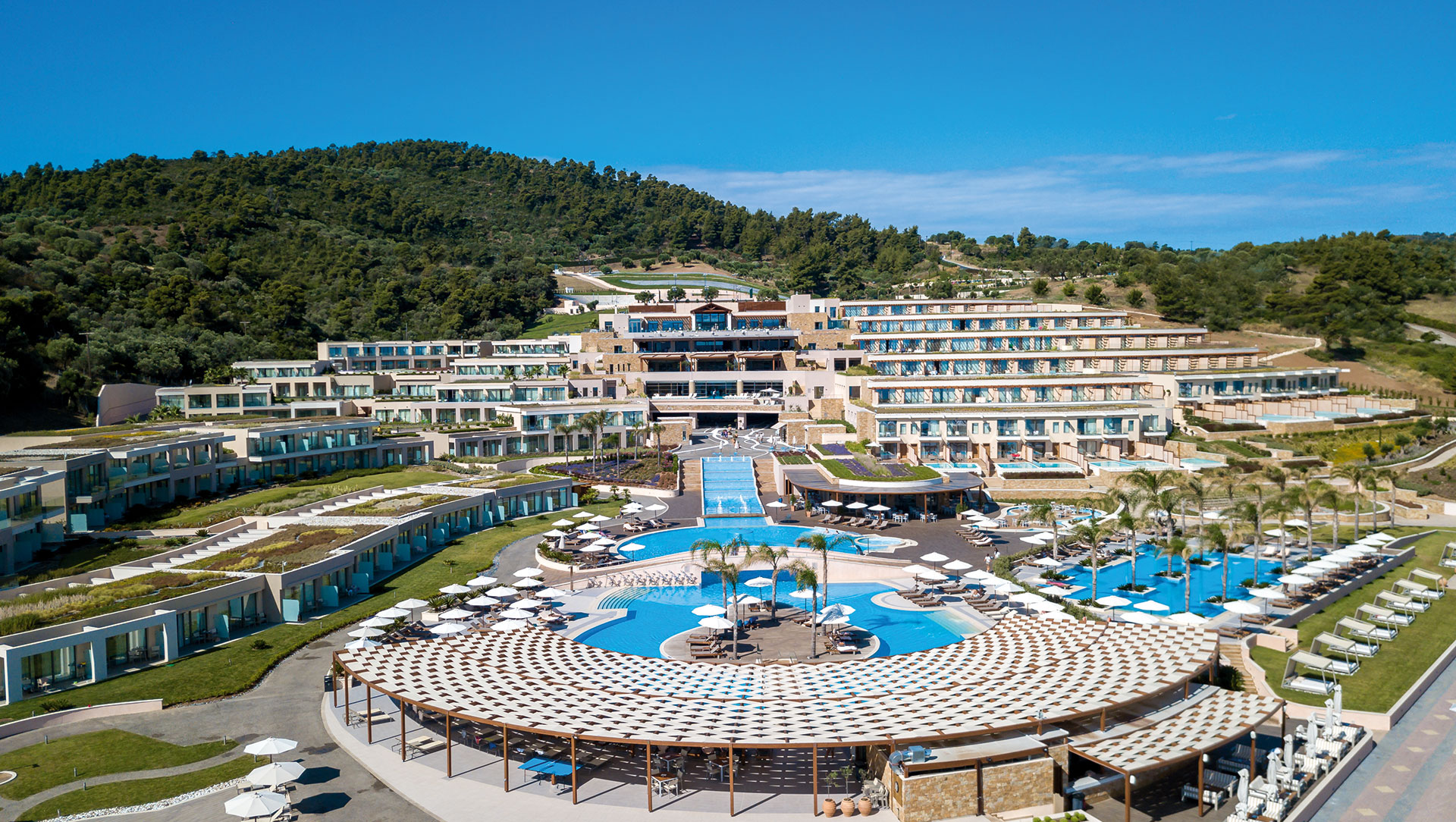 Aerial front view of tiered resort architecture with pools and palm trees