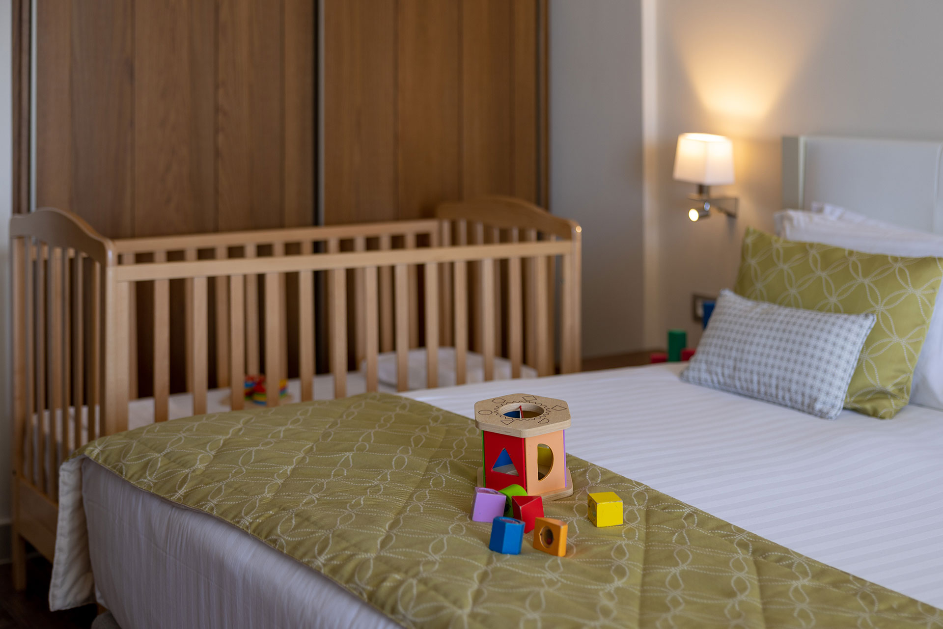 Family-friendly deluxe room with baby cot, colorful toys, and soft green bedding