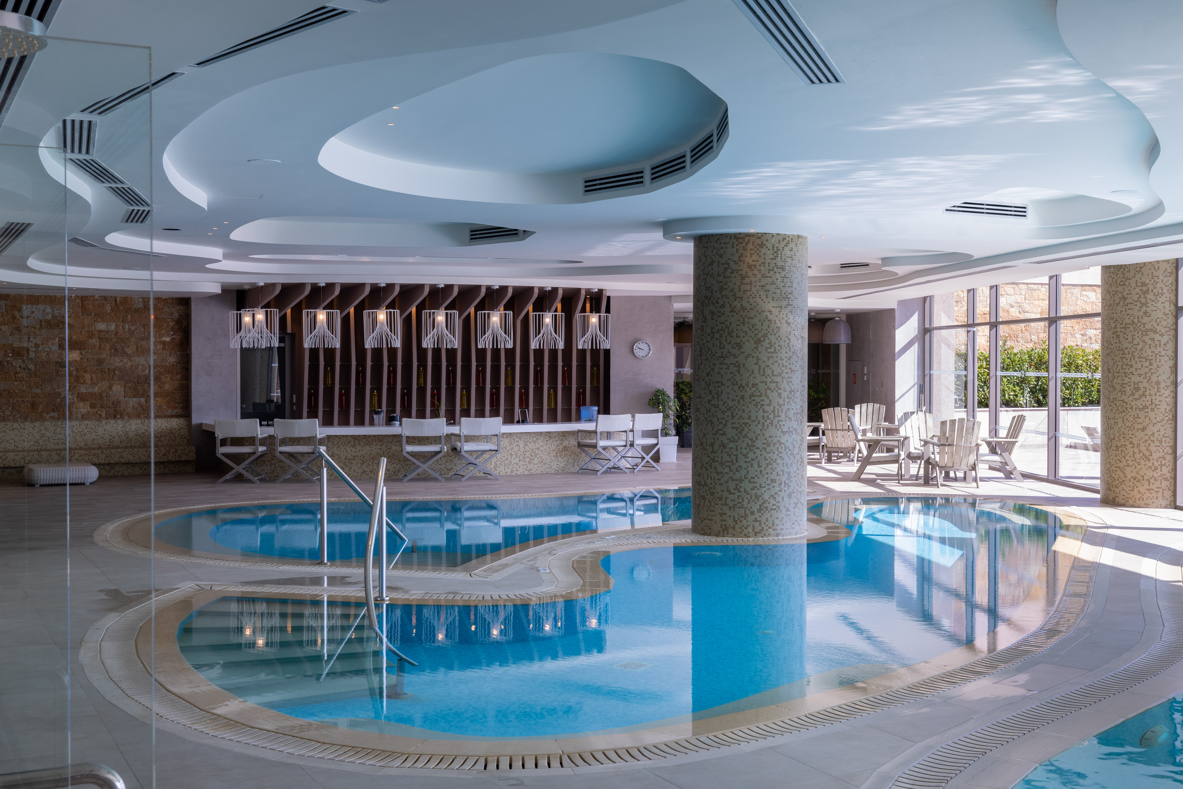 Elegant indoor pool area with curved design, lounge chairs and natural light