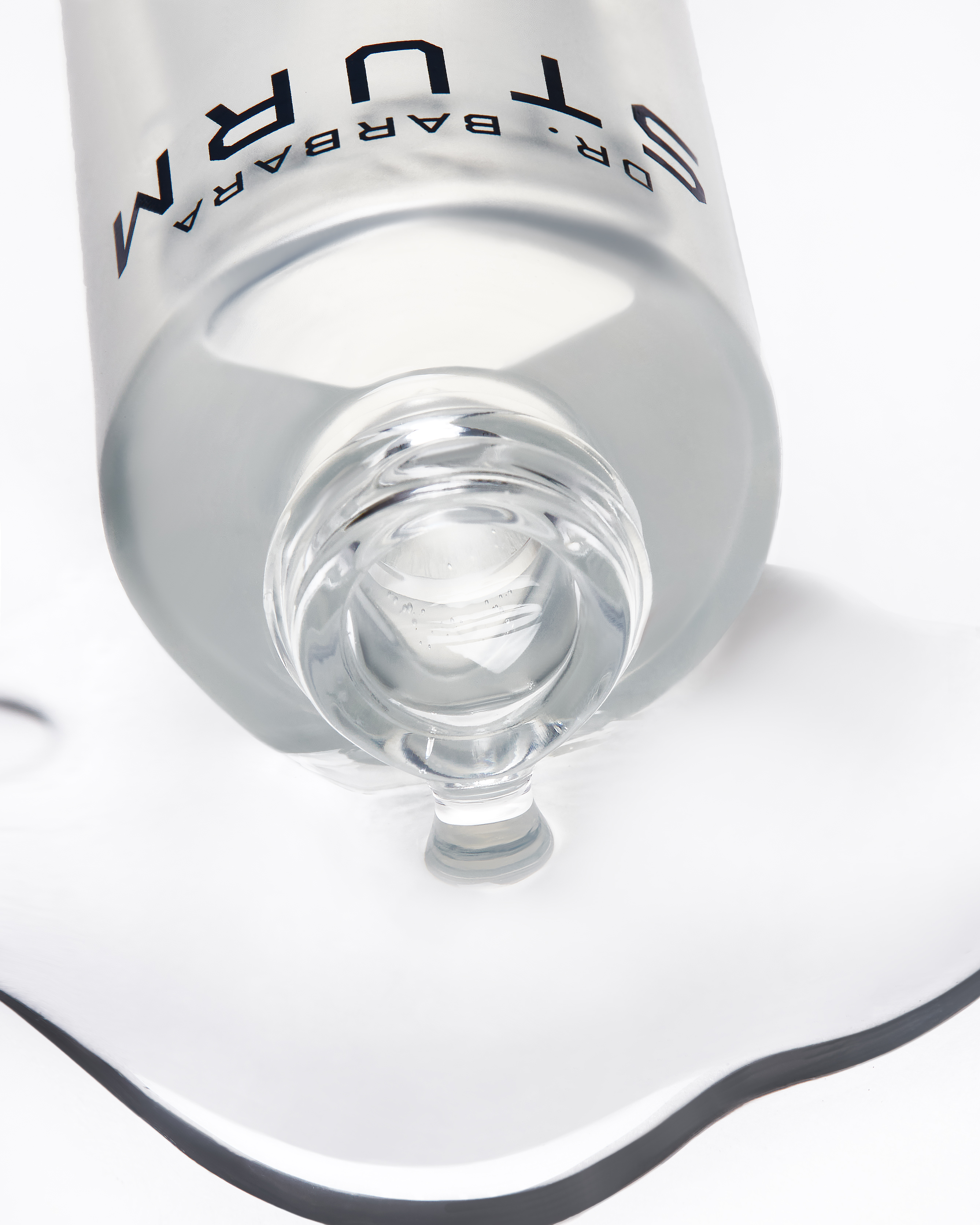 Open Dr. Barbara Sturm serum bottle with liquid spilling gently on white surface