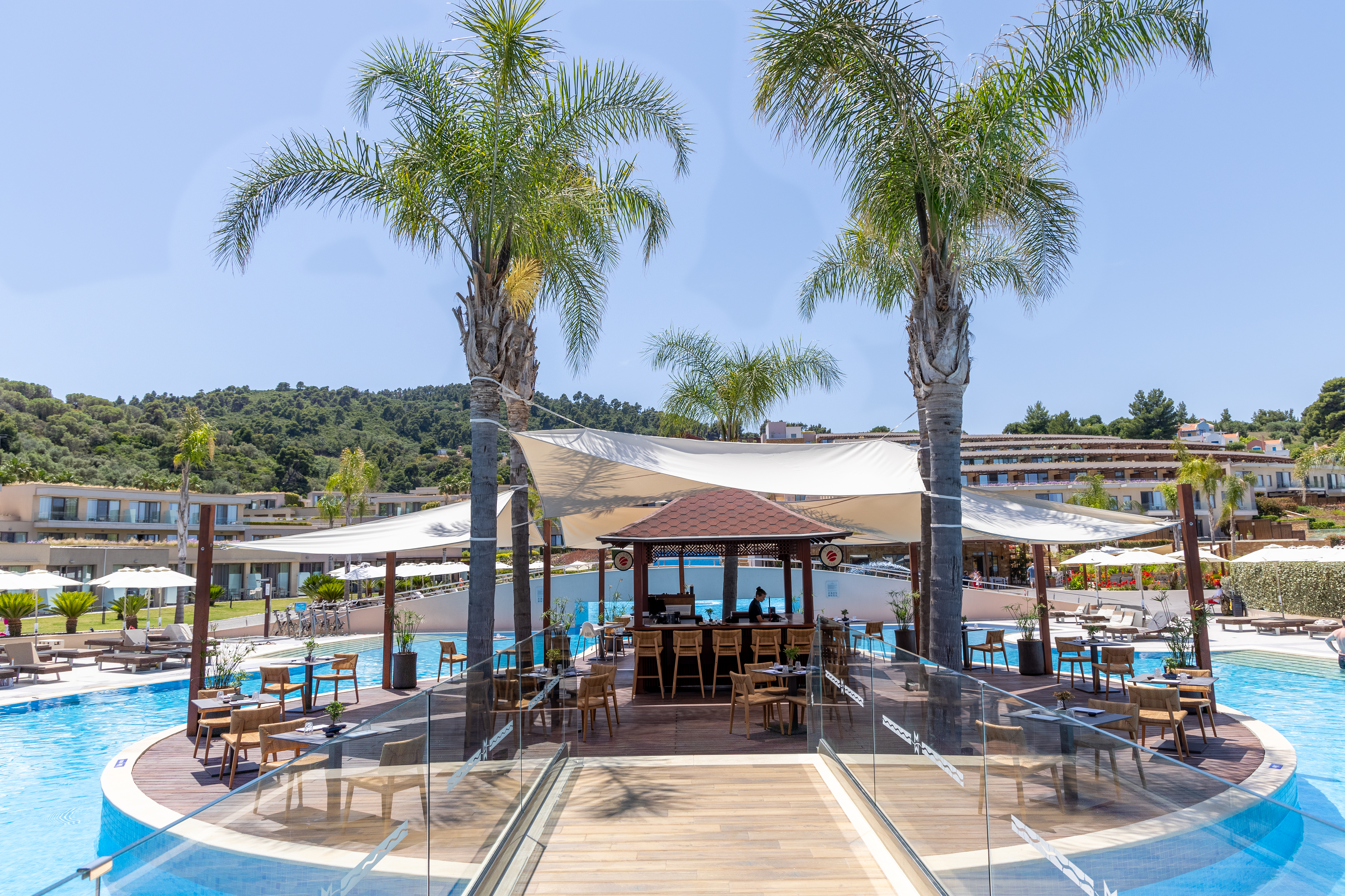 Poolside bar surrounded by palm trees and lounge chairs under sunny skies