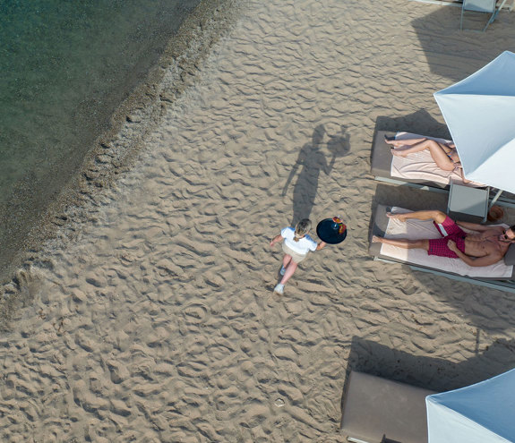 Top down view of a waitress serving drinks to a couple enjoying the sandy beach and clear blue sea