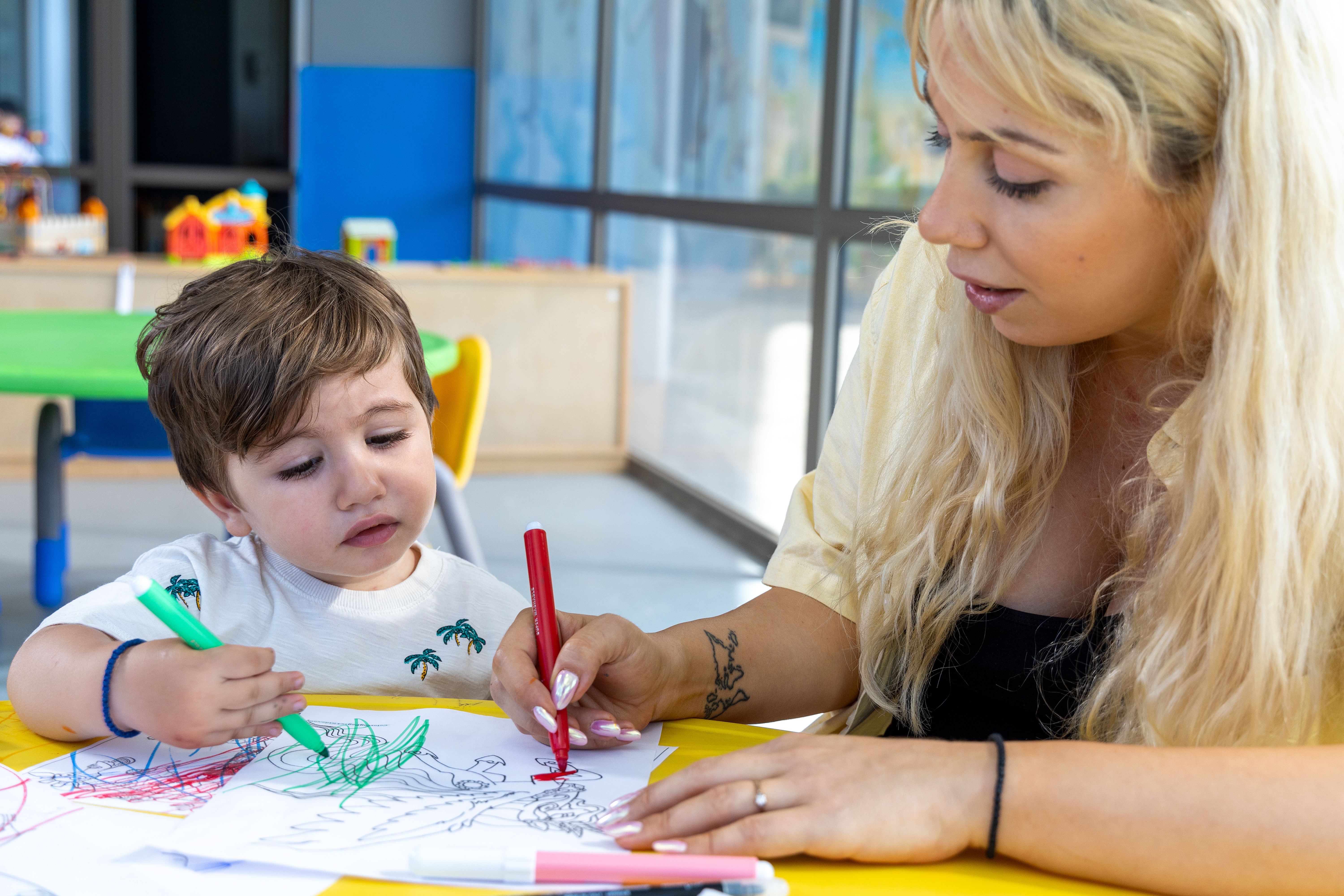 Mother showing her kid how to paint on a table in Kids Planet indoor playground