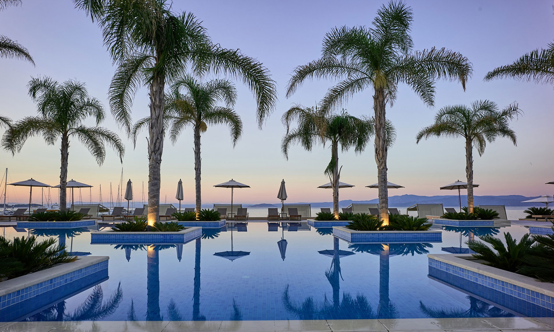 Serene poolside view with palm trees and loungers overlooking the sea at sunset