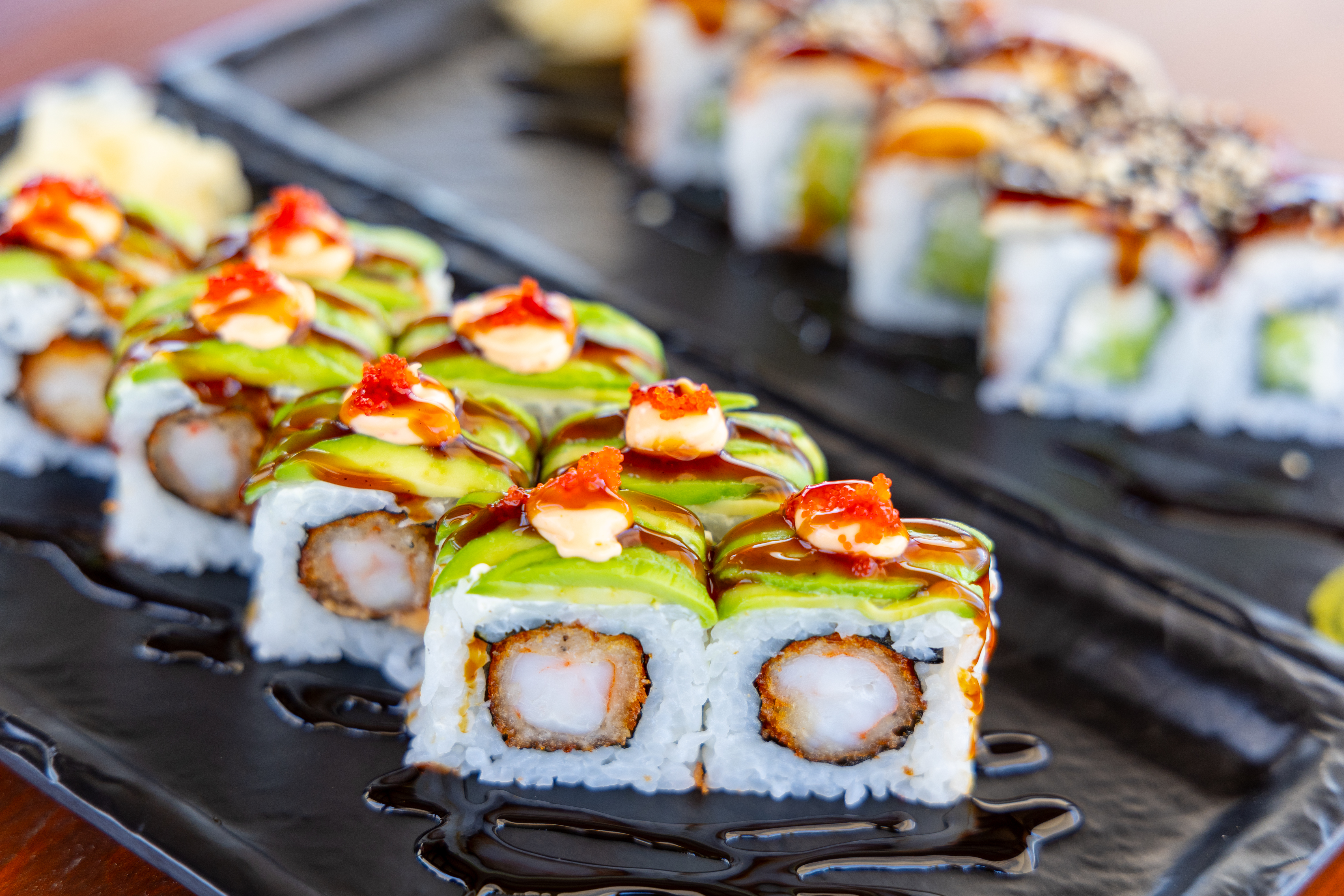 Close-up of colorful sushi rolls topped with avocado, spicy mayo, and sauce drizzle