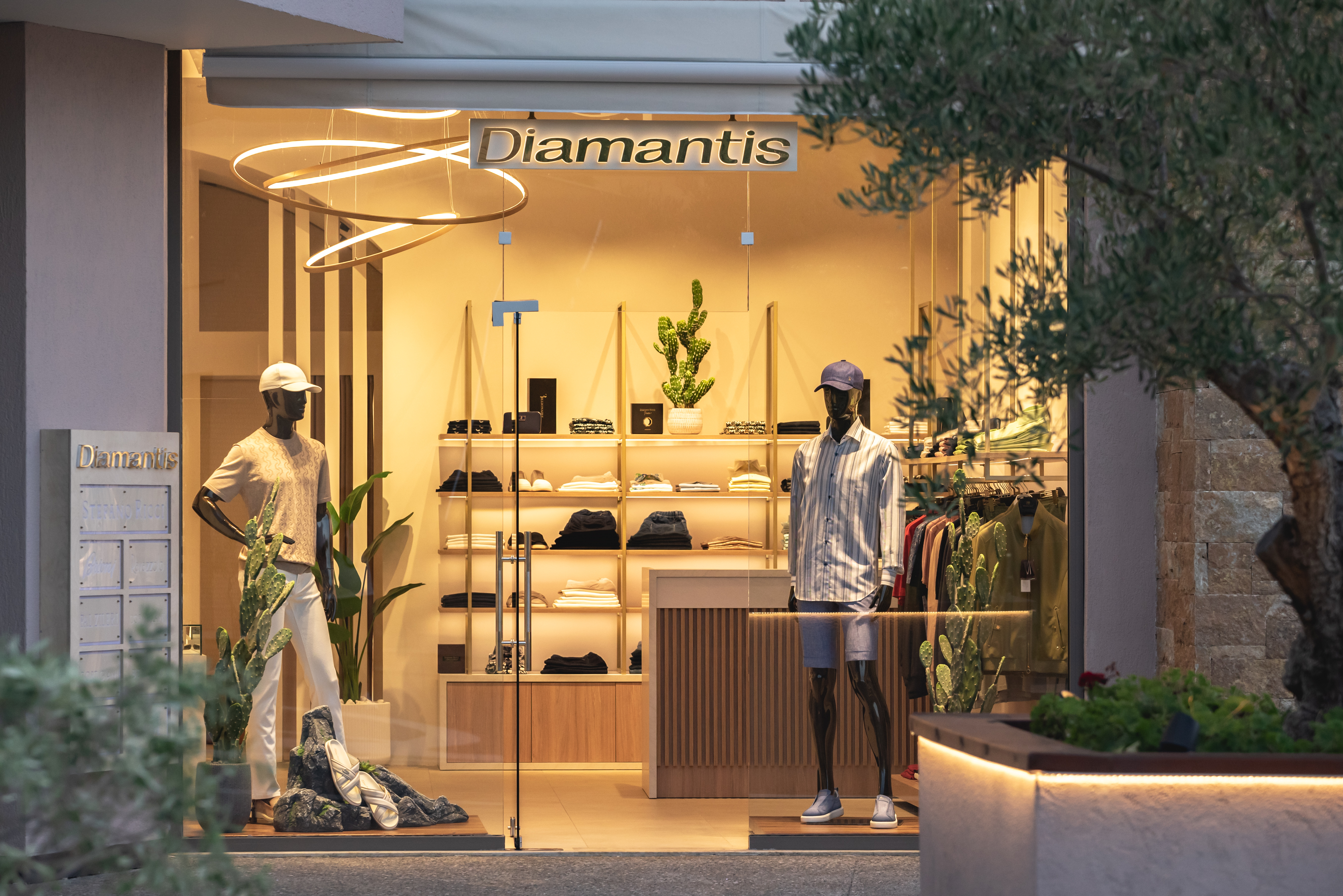 Evening view of Diamantis Boutique storefront with warm lighting, modern interior, and summer menswear