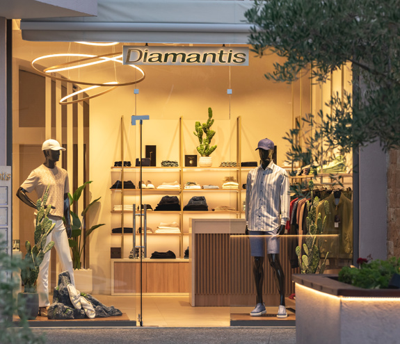 Evening view of Diamantis Boutique storefront with warm lighting, modern interior, and summer menswear
