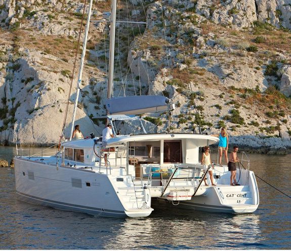 Luxury catamaran anchored by rocky coastline with guests relaxing on deck