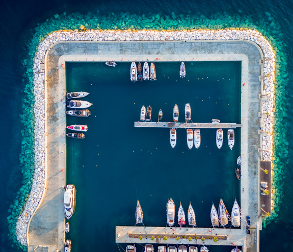 Aerial top-down view of a luxury marina with yachts moored along bright turquoise waters