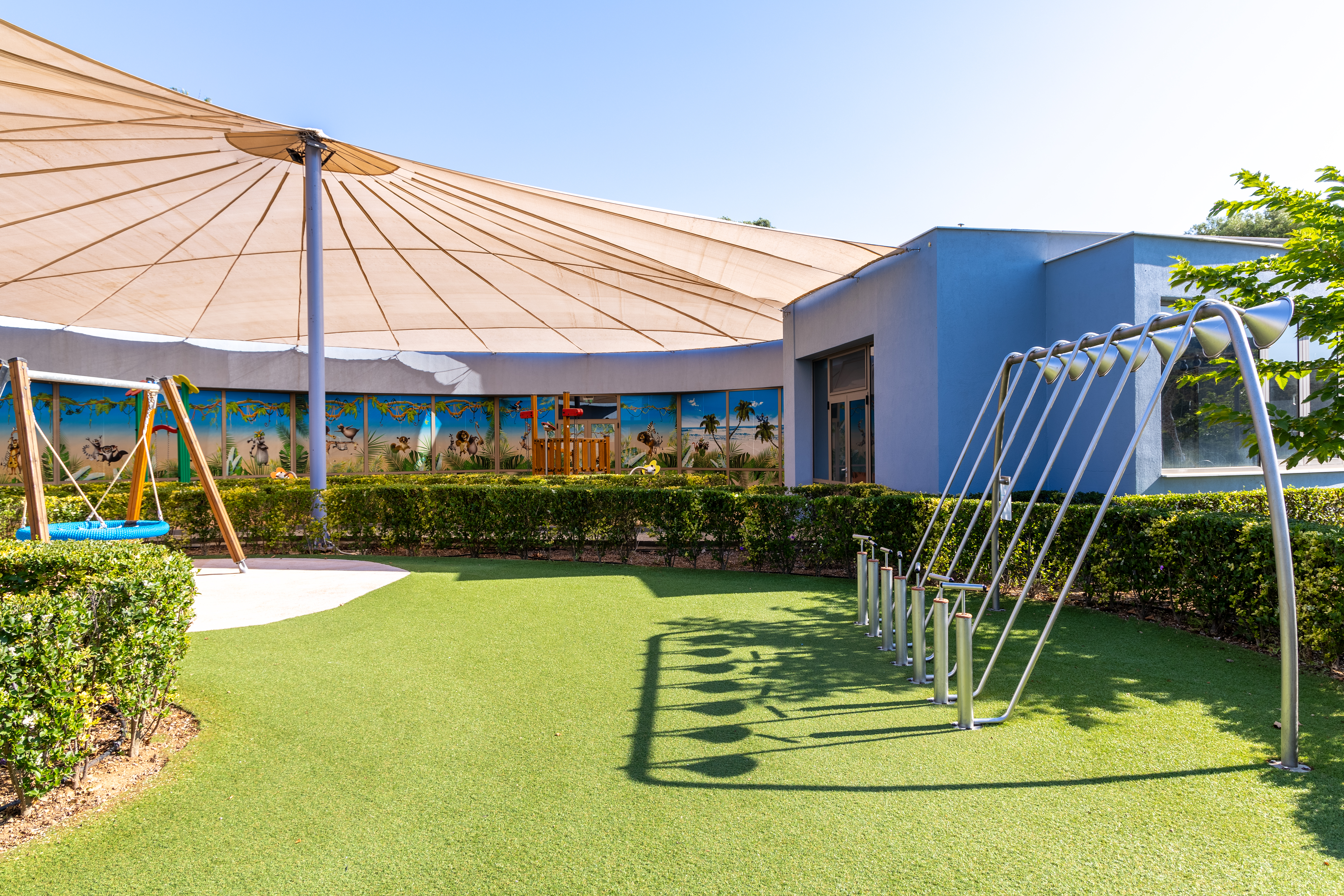 Shaded outdoor play area with swings and climbing equipment at Kids Planet