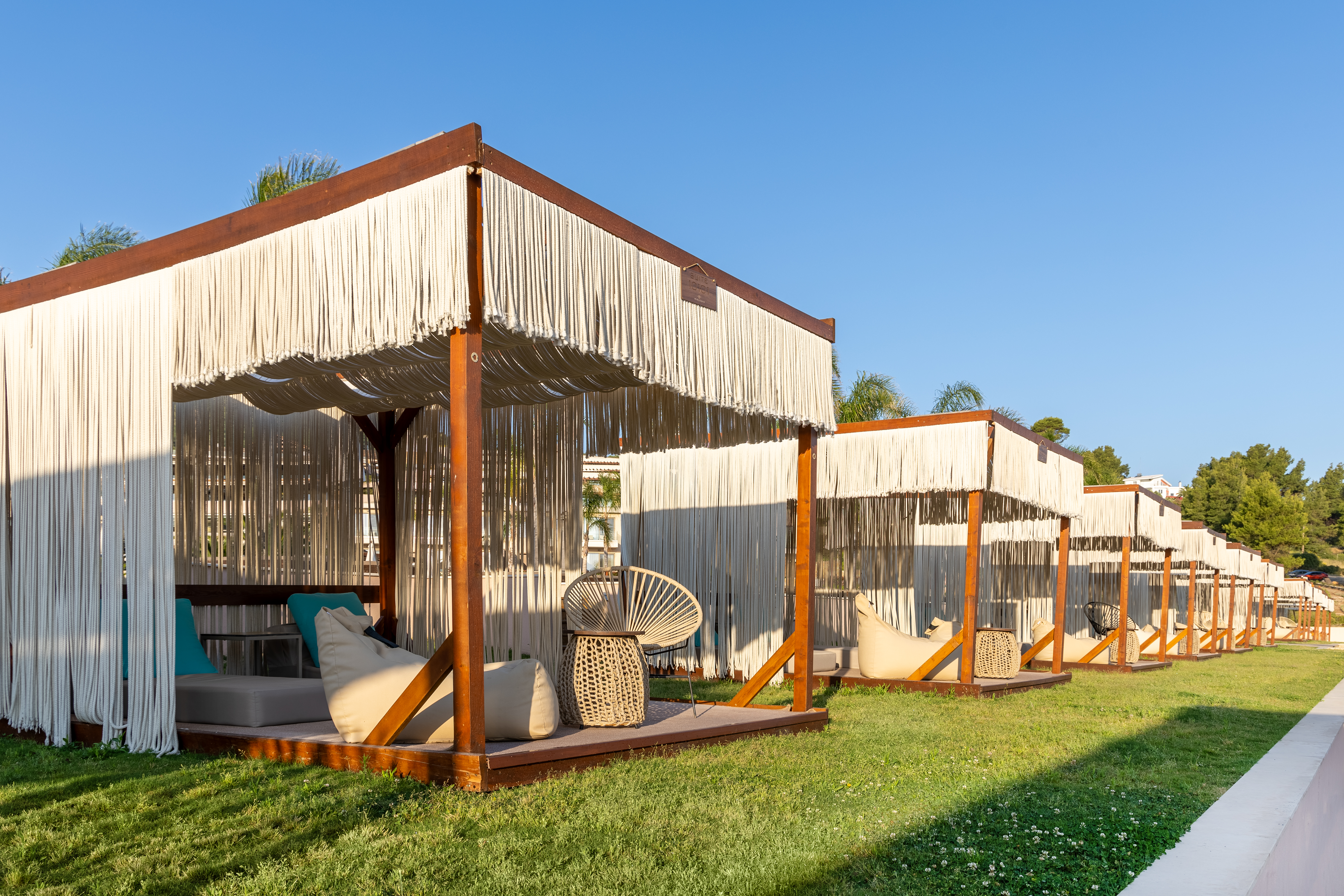 Row of elegant cabanas with fringe curtains and cushioned loungers under clear blue skies