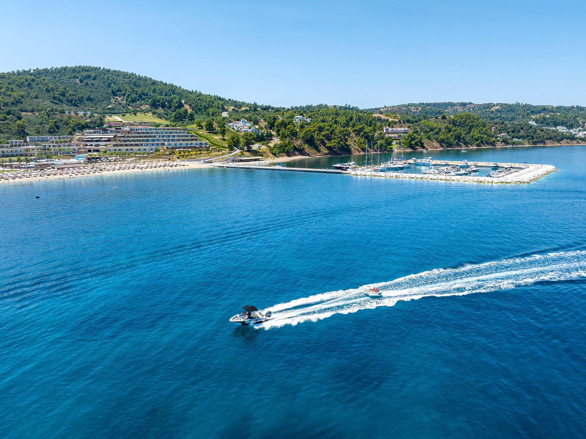 Speedboat towing guests on an inflatable ride across turquoise waters near the marina and beach