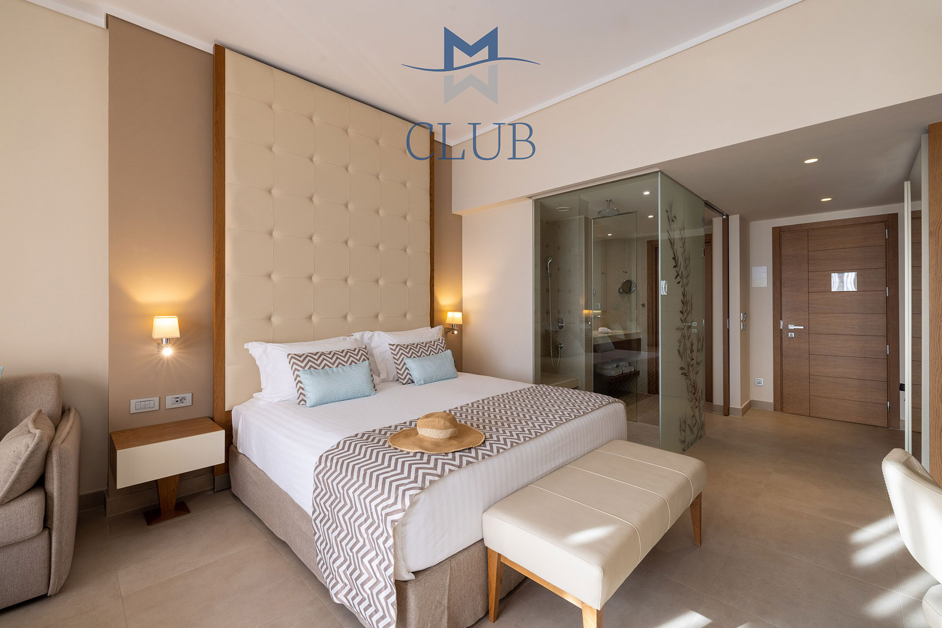 Club sea view room with king size bed with wooden headboard, bedside table with warm lighting and bathroom 