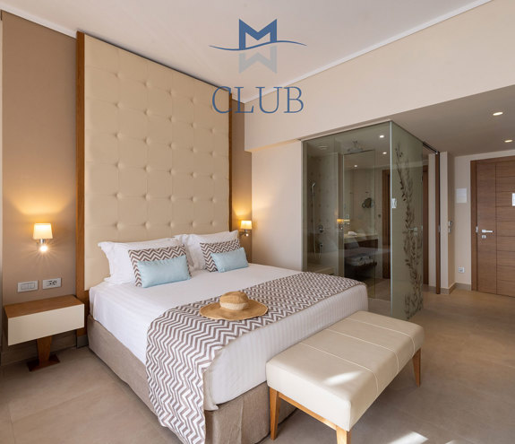 Club sea view room with king size bed with wooden headboard, bedside table with warm lighting and bathroom 
