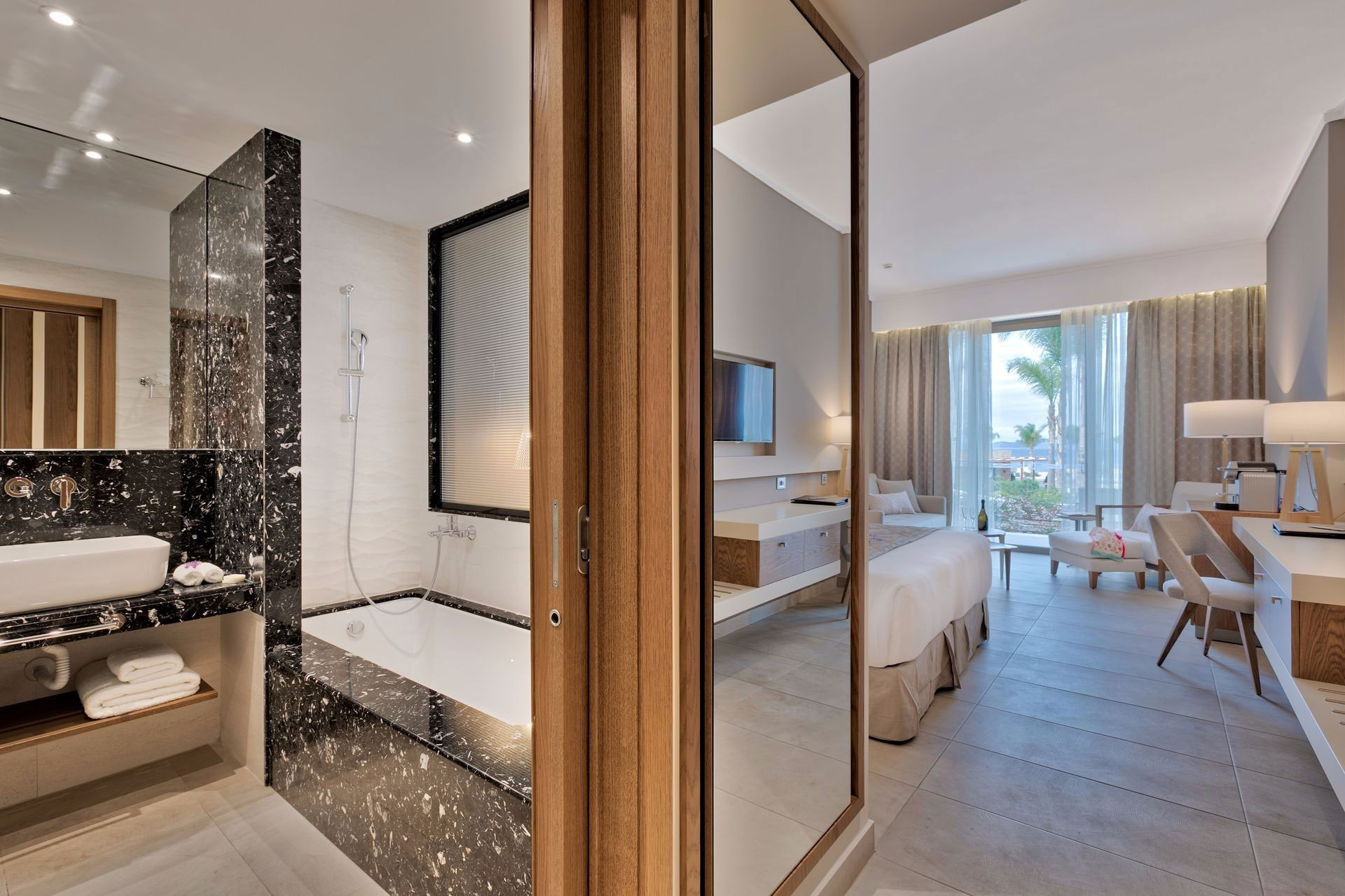 Spacious deluxe room's wide view, with elegant marble bathroom, bedroom and seating area beside the balcony door