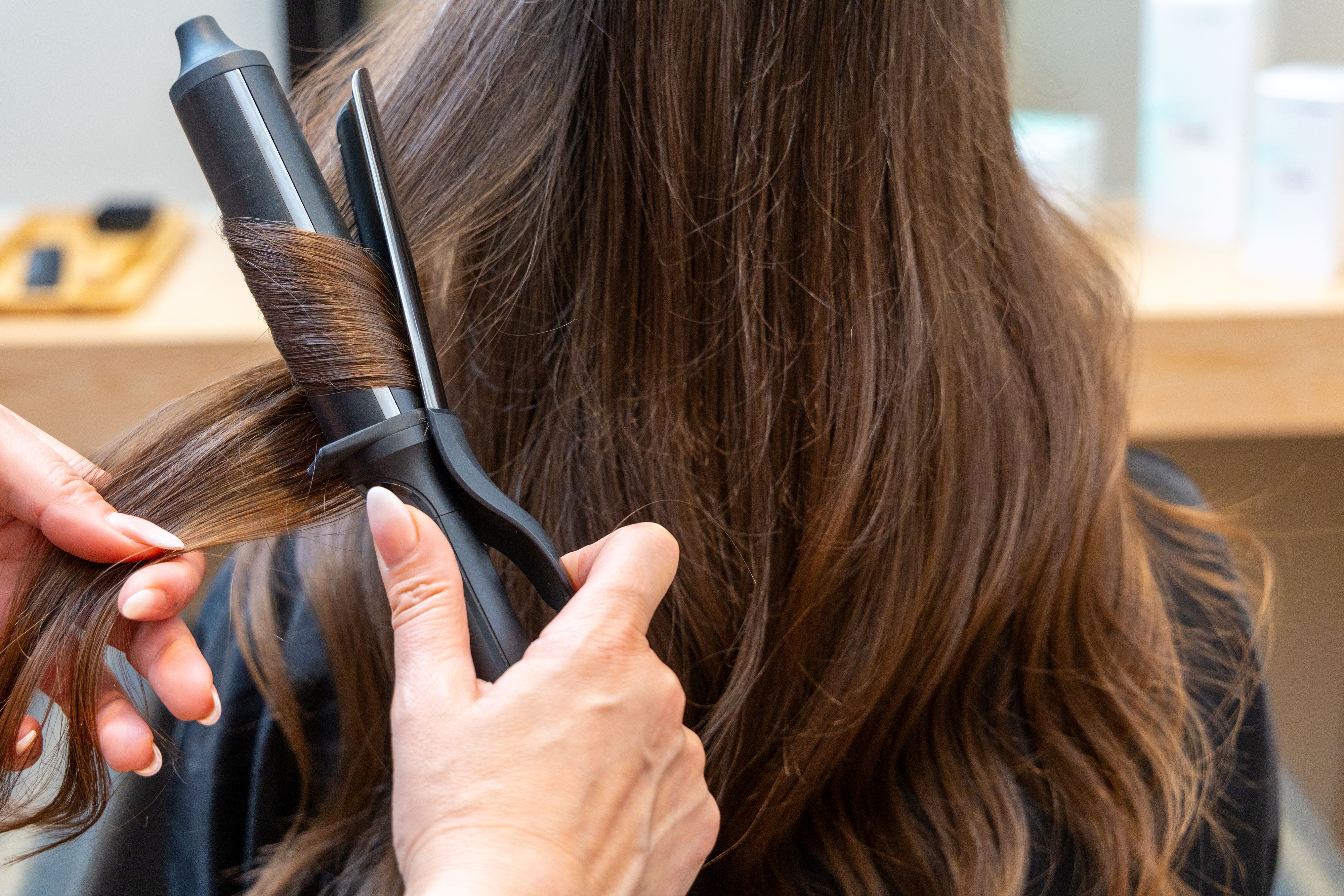 Hairstylist curling long brown hair with professional styling tool