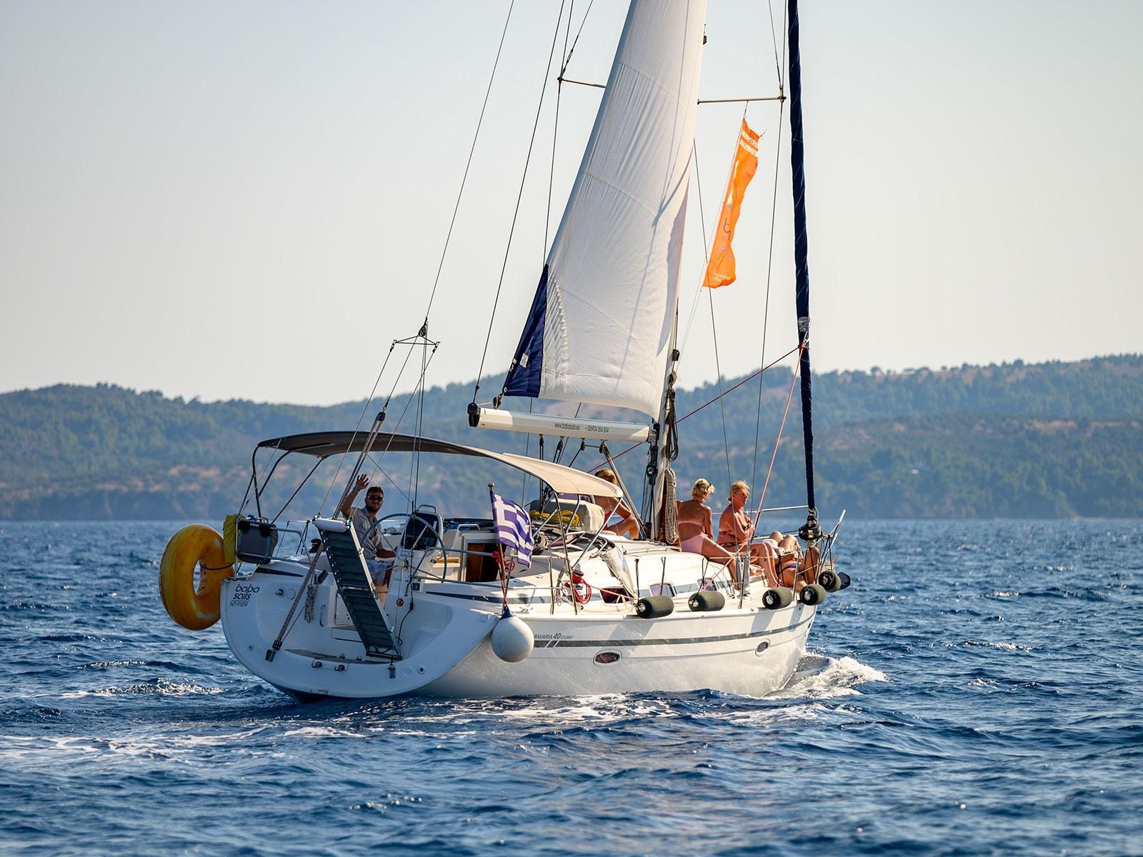 A white sailing yacht cruising on calm blue water, with people relaxing on deck under the sun