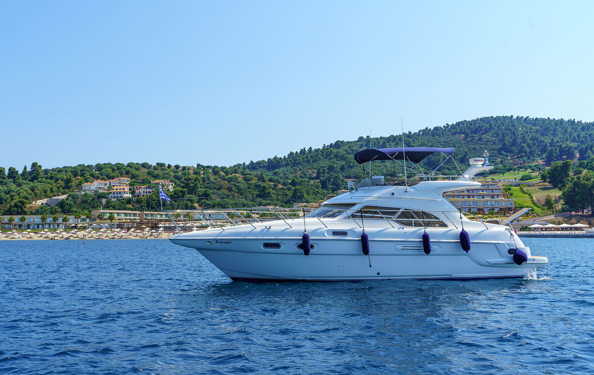 Luxury yacht sailing near the resort shoreline with clear blue sea and green hills