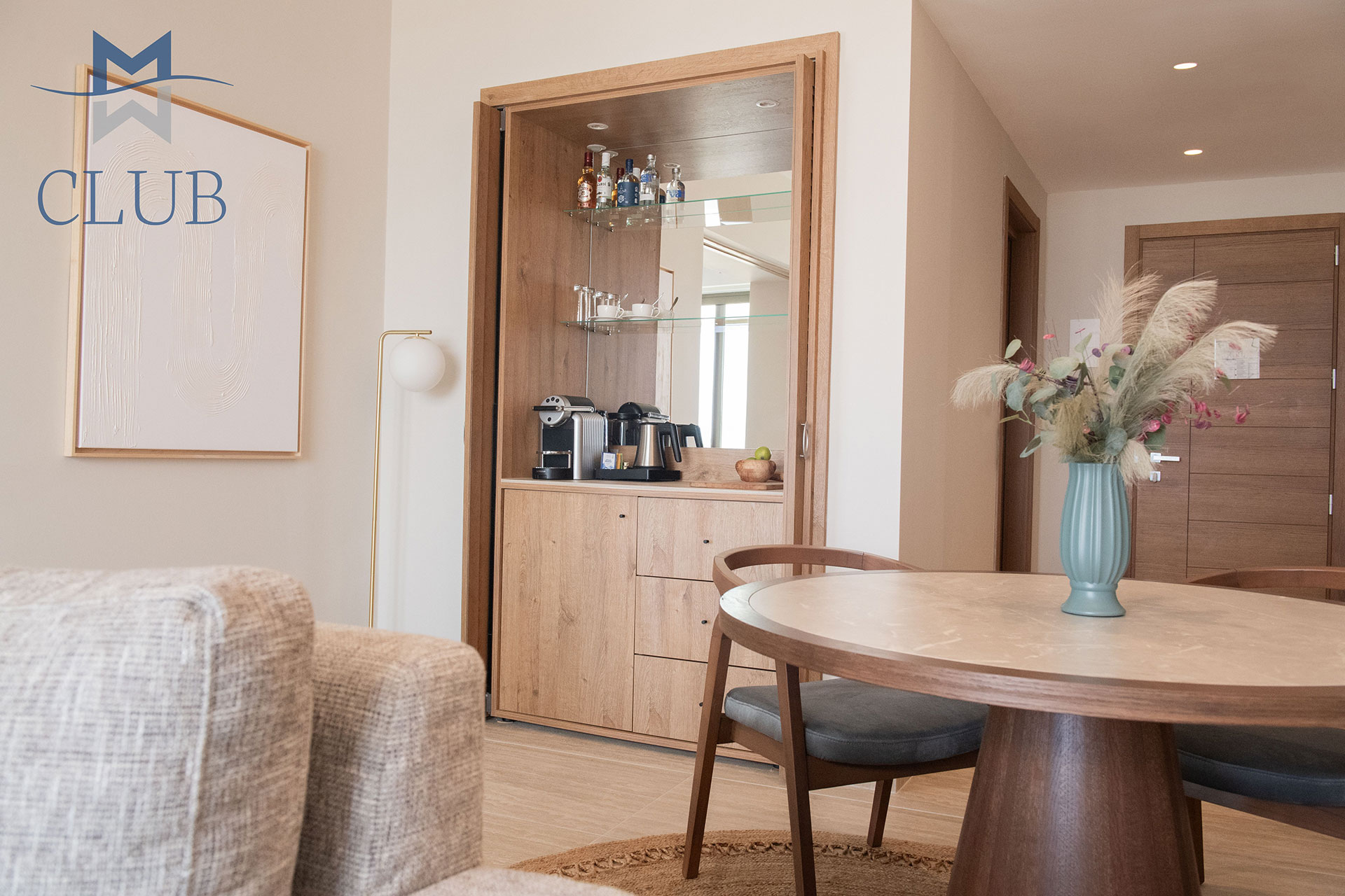 Living area in suite featuring a wooden dining table, minibar with coffee machine and warm-toned furnishing