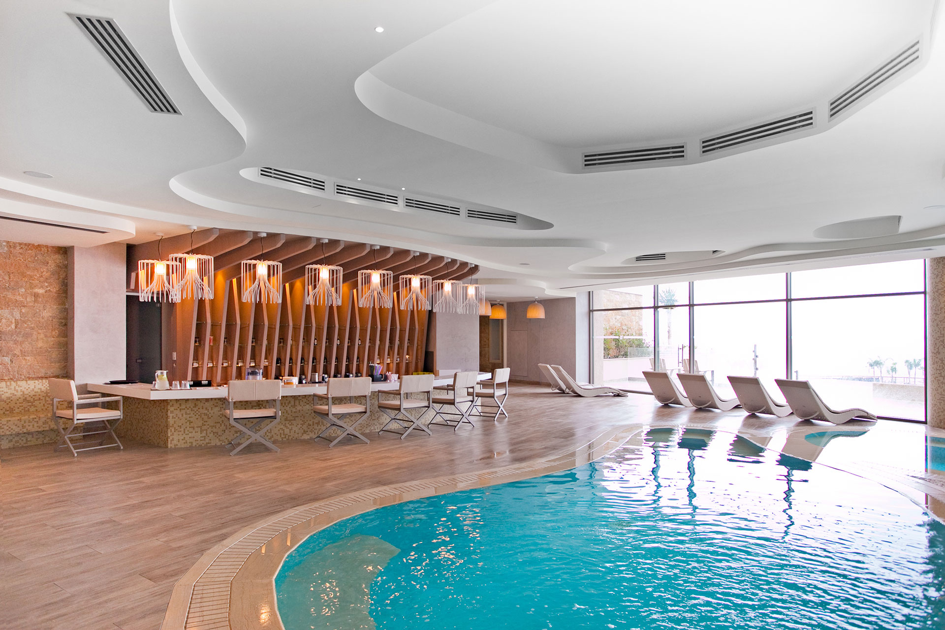 Indoor spa lounge with stylish bar, designer lighting, and poolside loungers