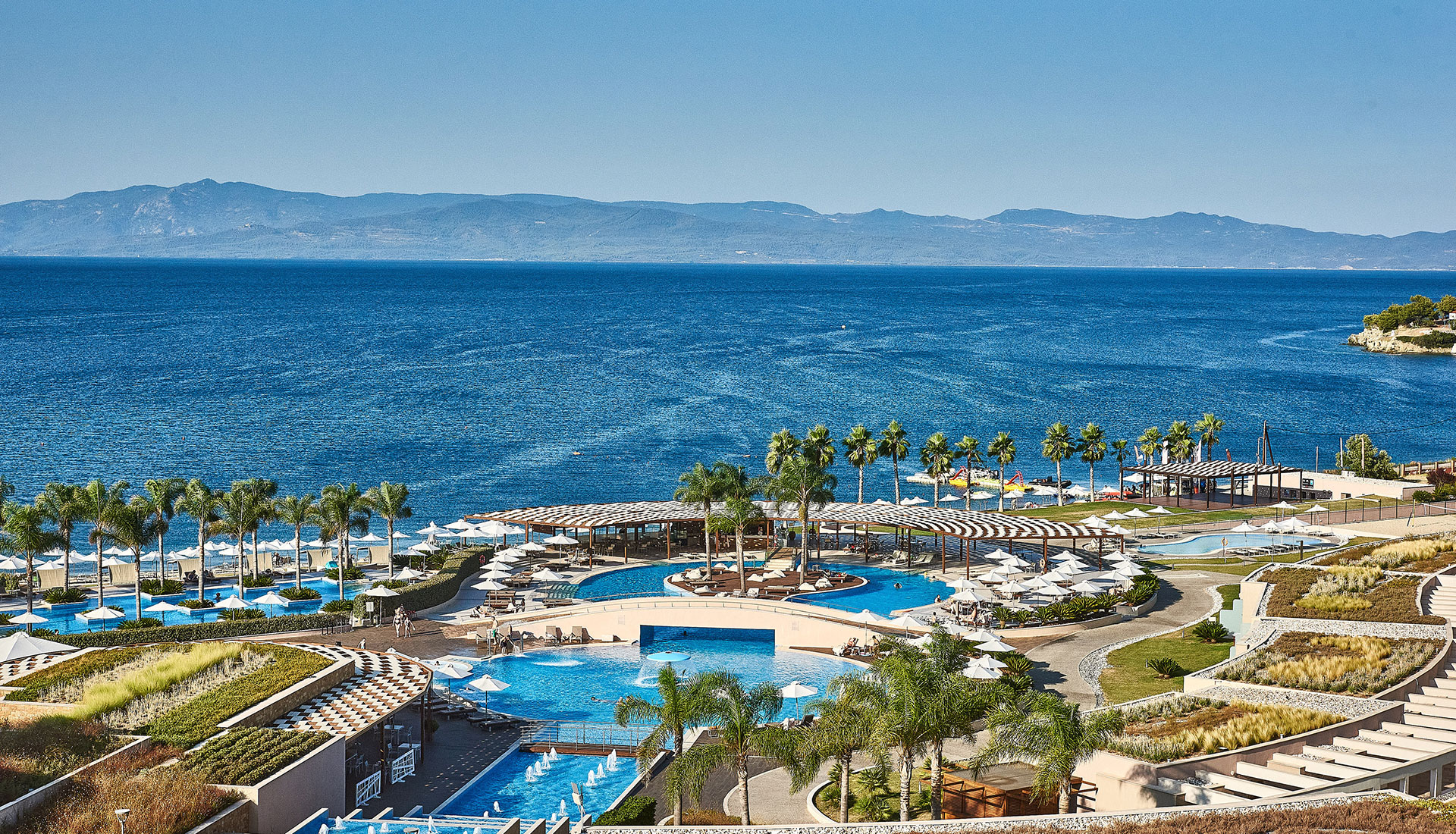 Panoramic view of resort pools, palm trees and the deep blue Aegean Sea