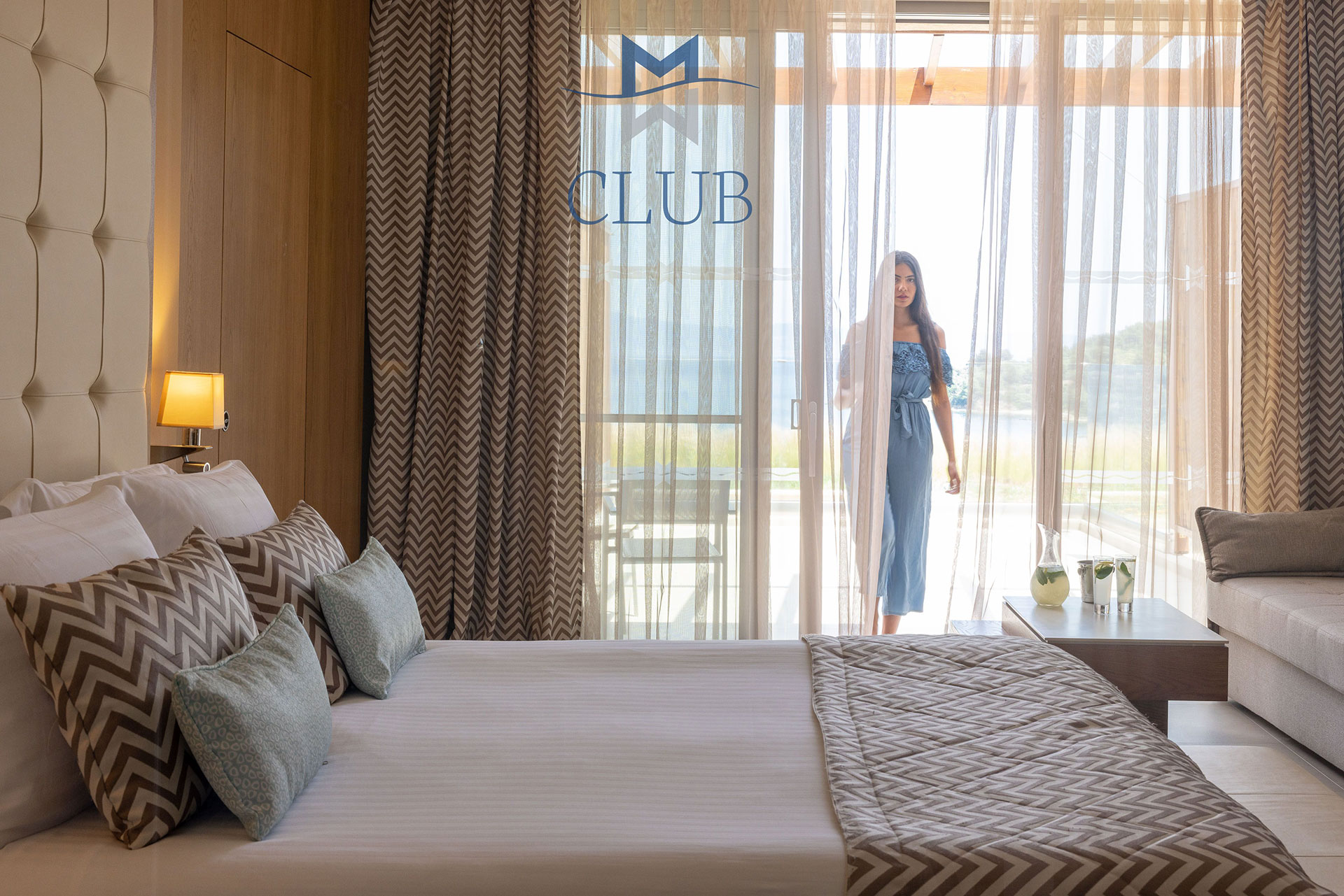 Club sea view room with king size bed, seating area and woman getting inside the room from private terrace