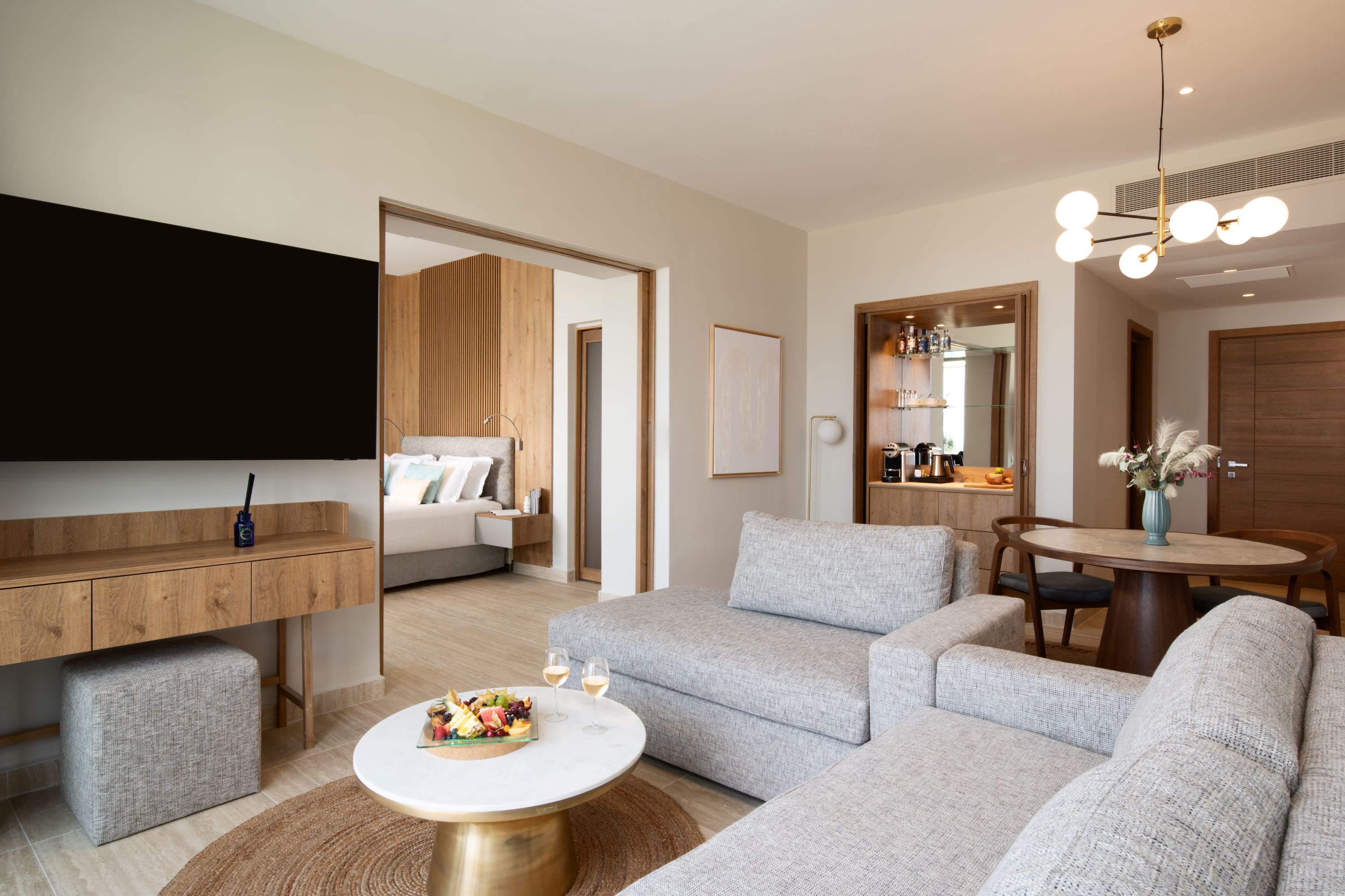 Spacious living area of the suite with cozy setup, dining table, minibar, and wall mounted TV