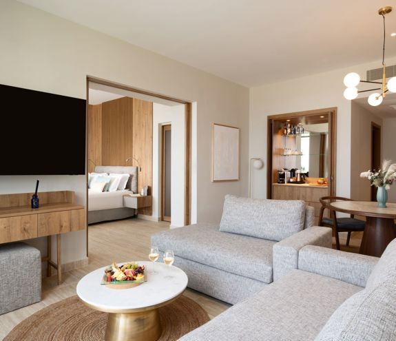 Spacious living area of the suite with cozy setup, dining table, minibar, and wall mounted TV