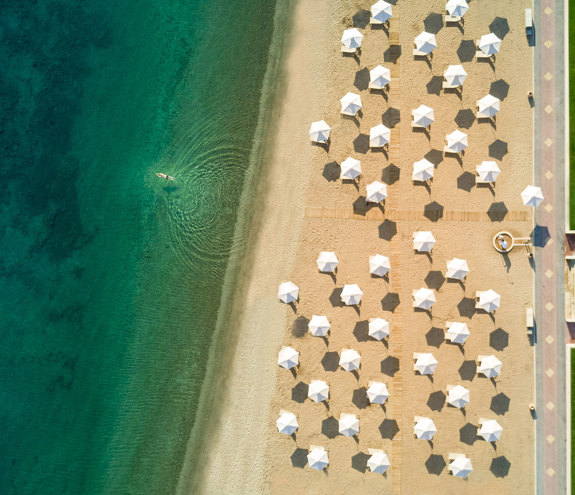 Aerial view of sandy beach with white umbrellas and crystal-clear turquoise sea
