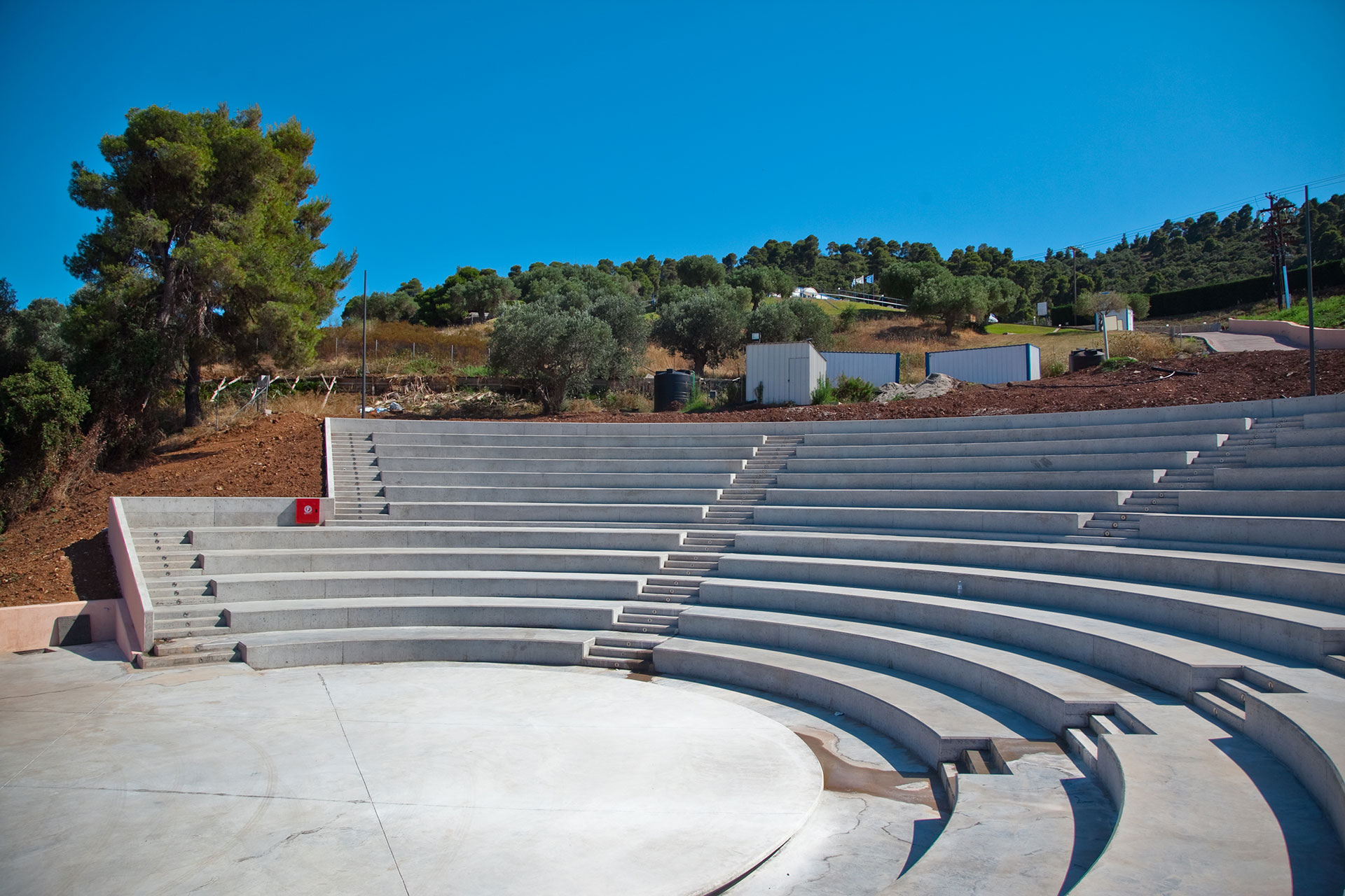 Concrete outdoor amphitheater surrounded by olive trees and hills