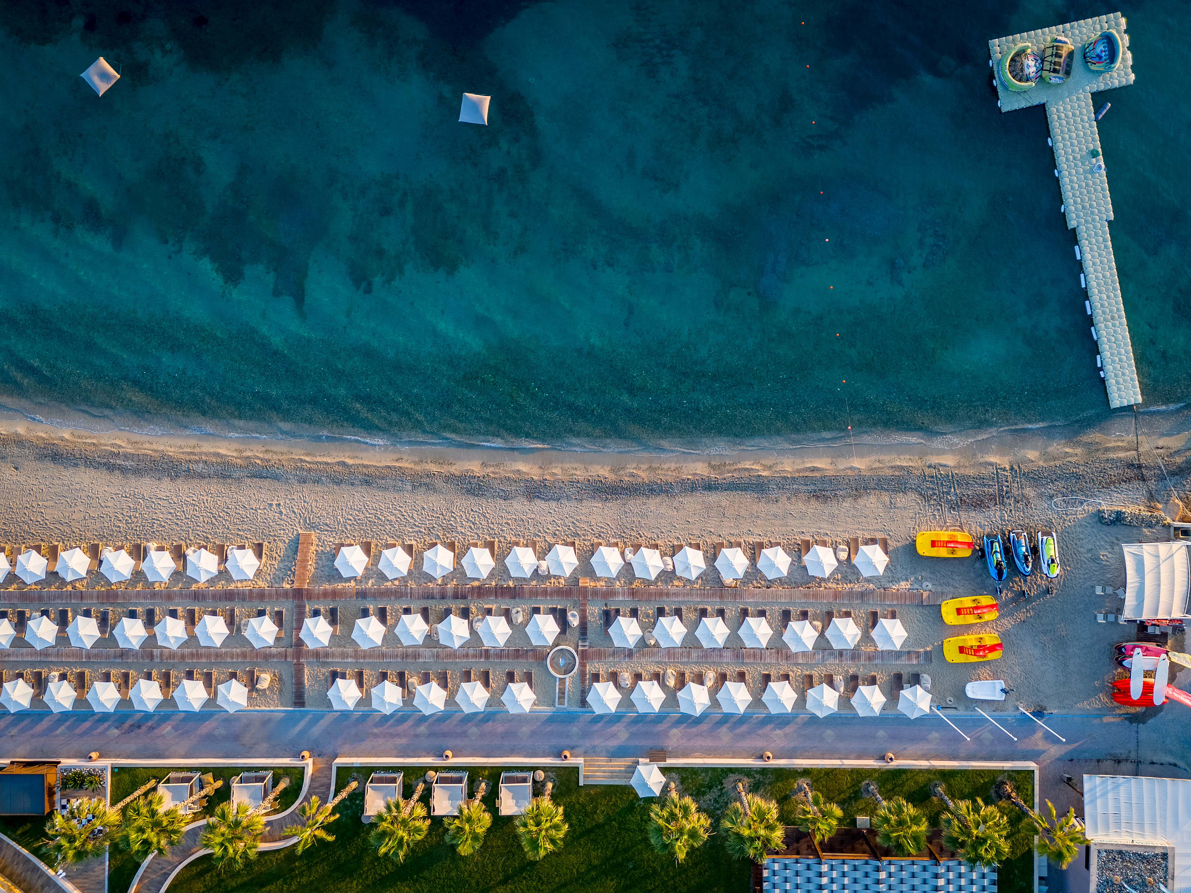 Aerial view of the beach with white umbrellas, cabanas, and crystal-clear turquoise water