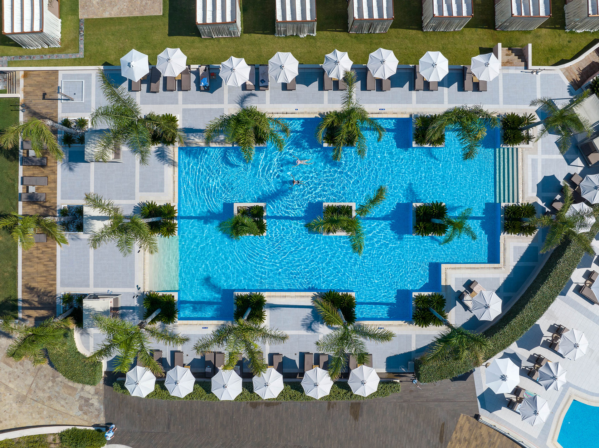 Aerial daytime view of the main swimming pool with palm trees, cabanas and sun loungers