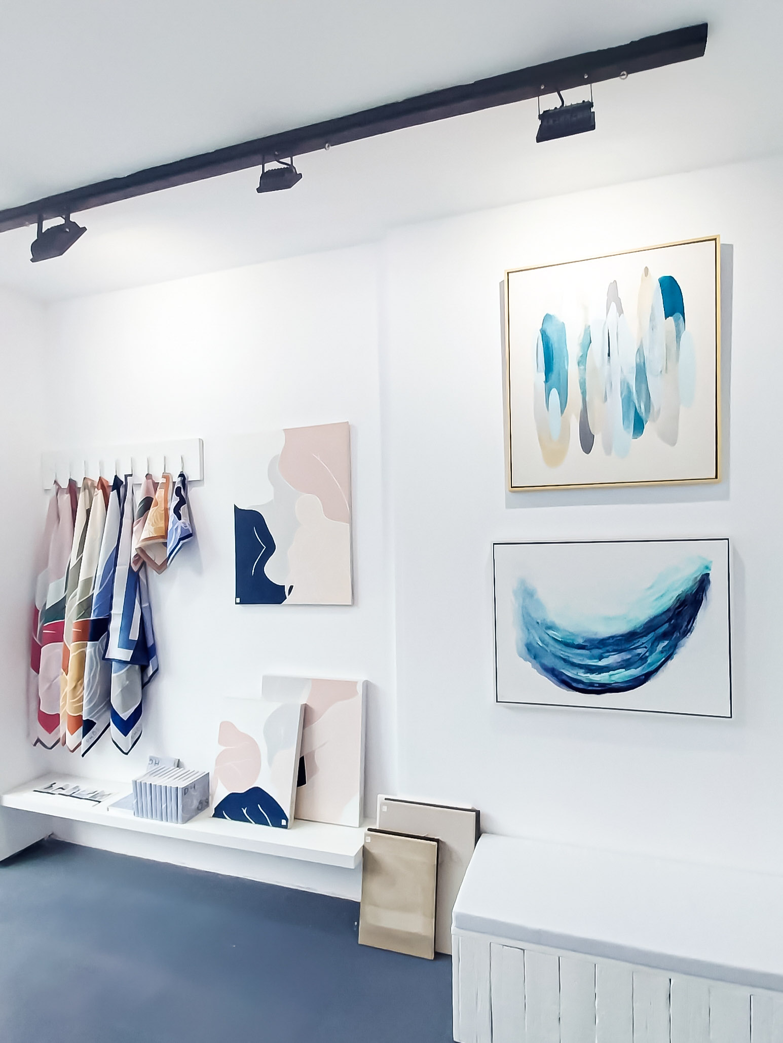 Abstract blue and beige paintings beside pastel colored scarves display