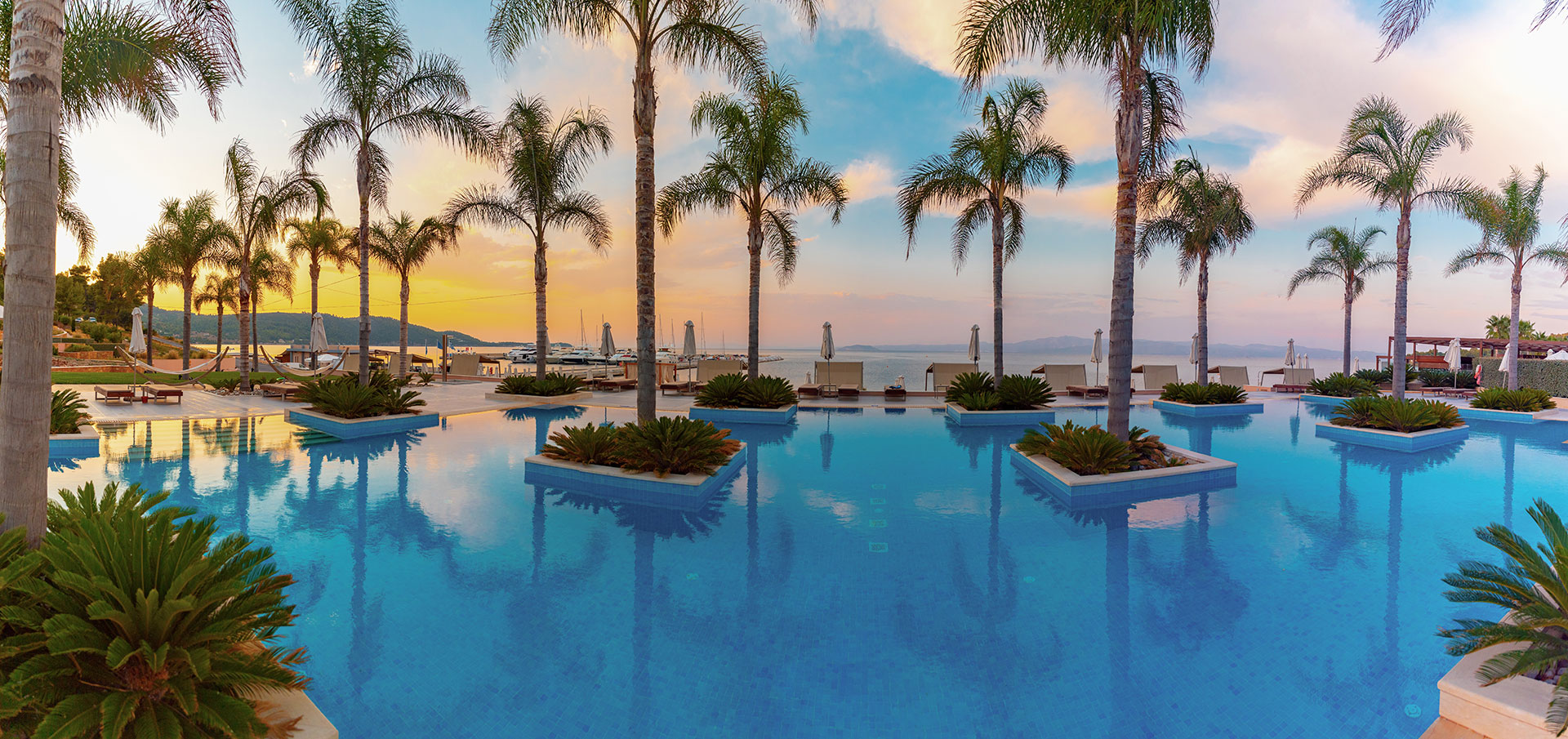 Relax pool surrounded by palm trees at sunset overlooking the Aegean Sea