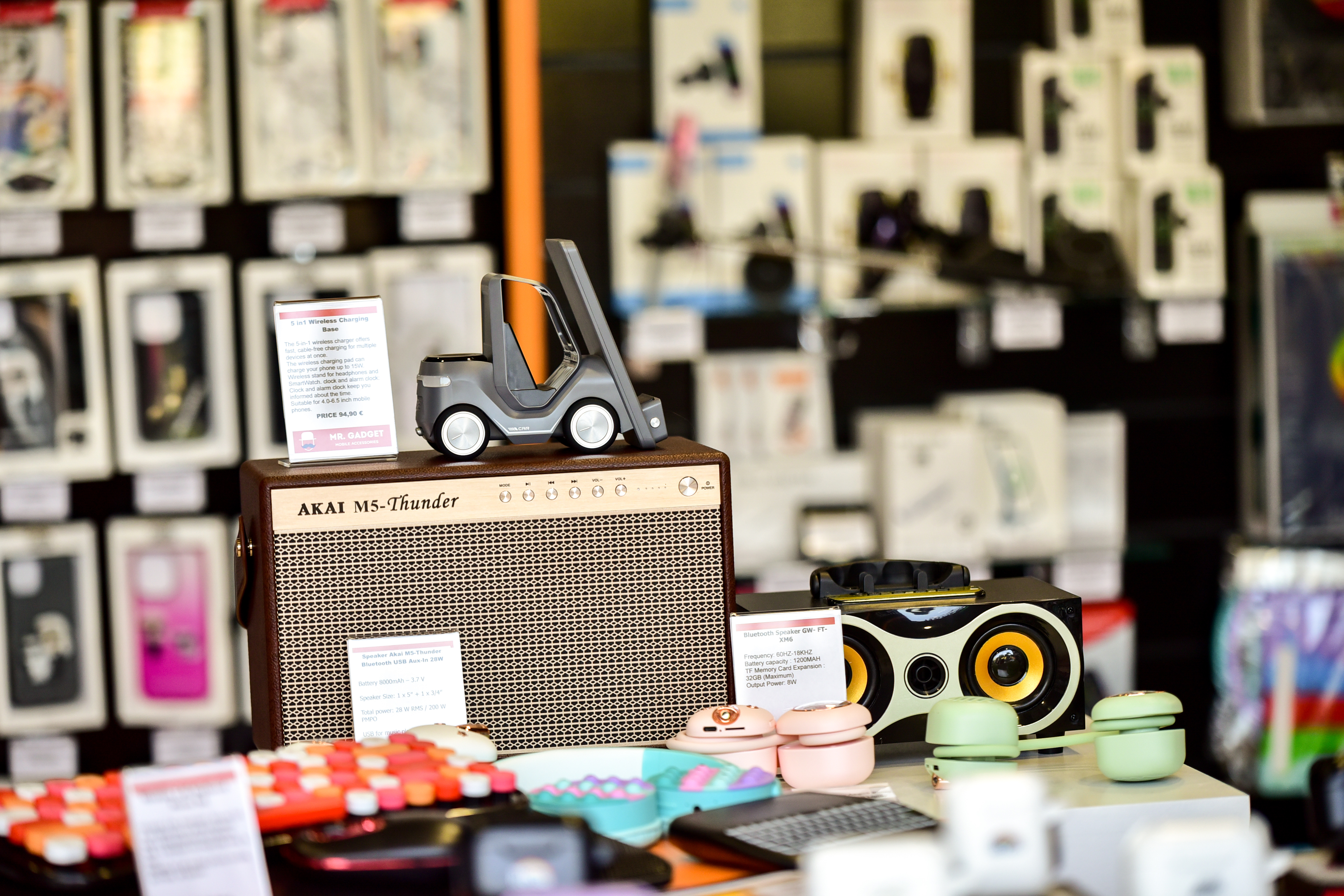 Display of Akai M5-Thunder Bluetooth speaker with wireless chargers and colorful portable gadgets