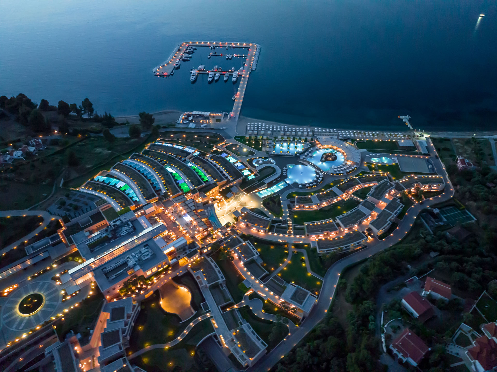 Aerial night view of the illuminated resort and marina reflecting on the calm Aegean Sea