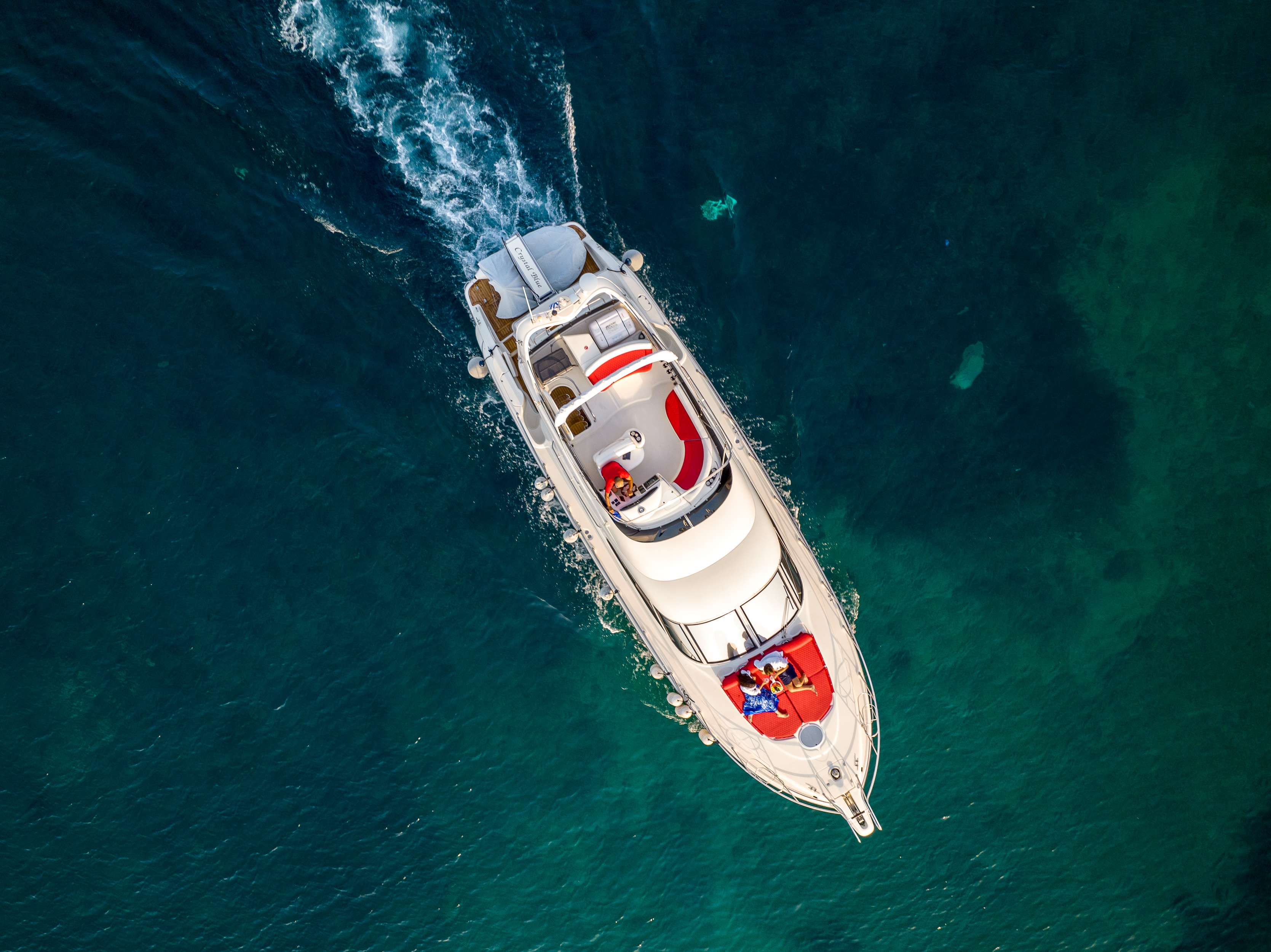 Couple relaxing on a luxury yacht cruising over clear turquoise water, viewed from above