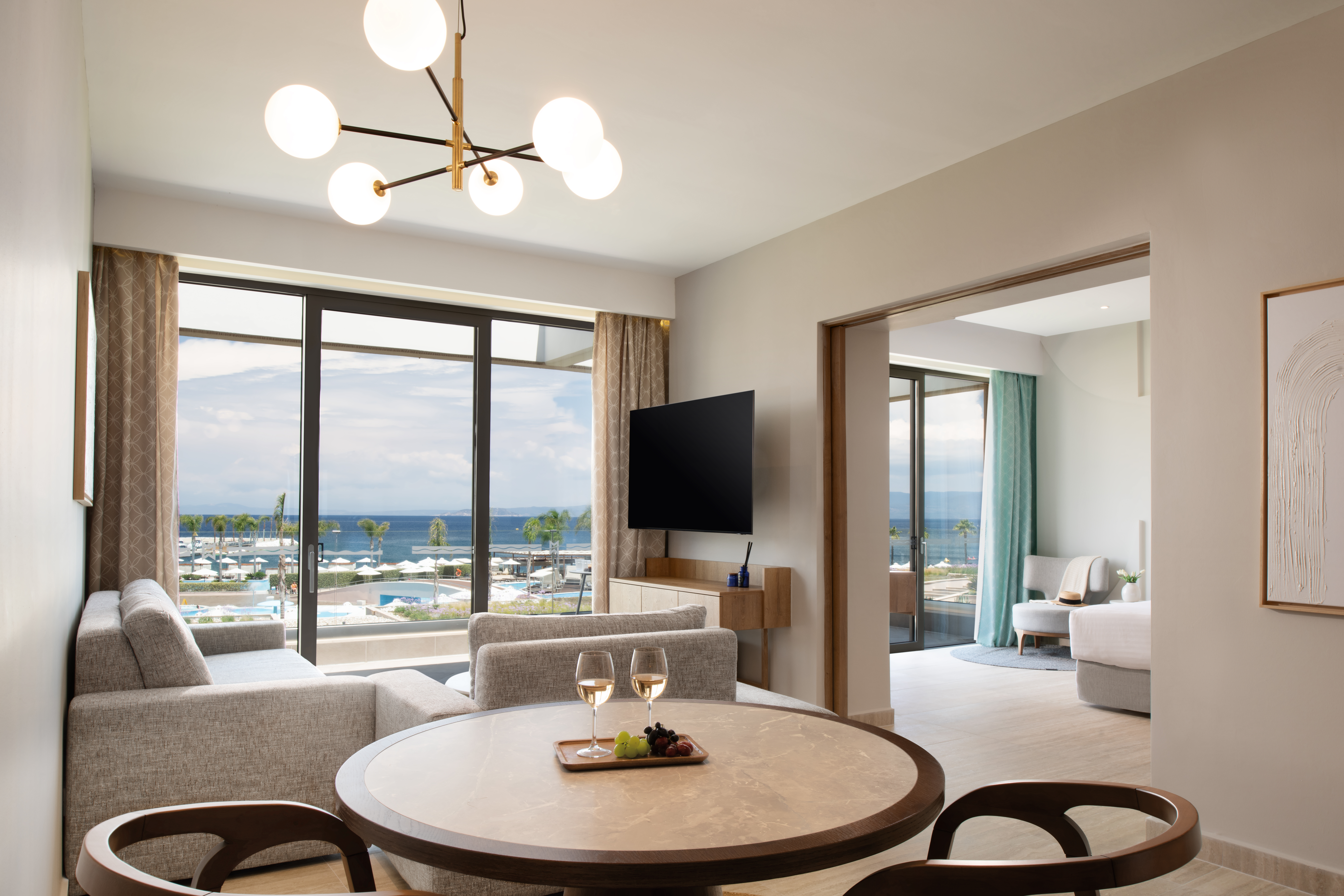 Elegant living area of the suite with modern furnishing and glass doors overlooking the resort and the sea
