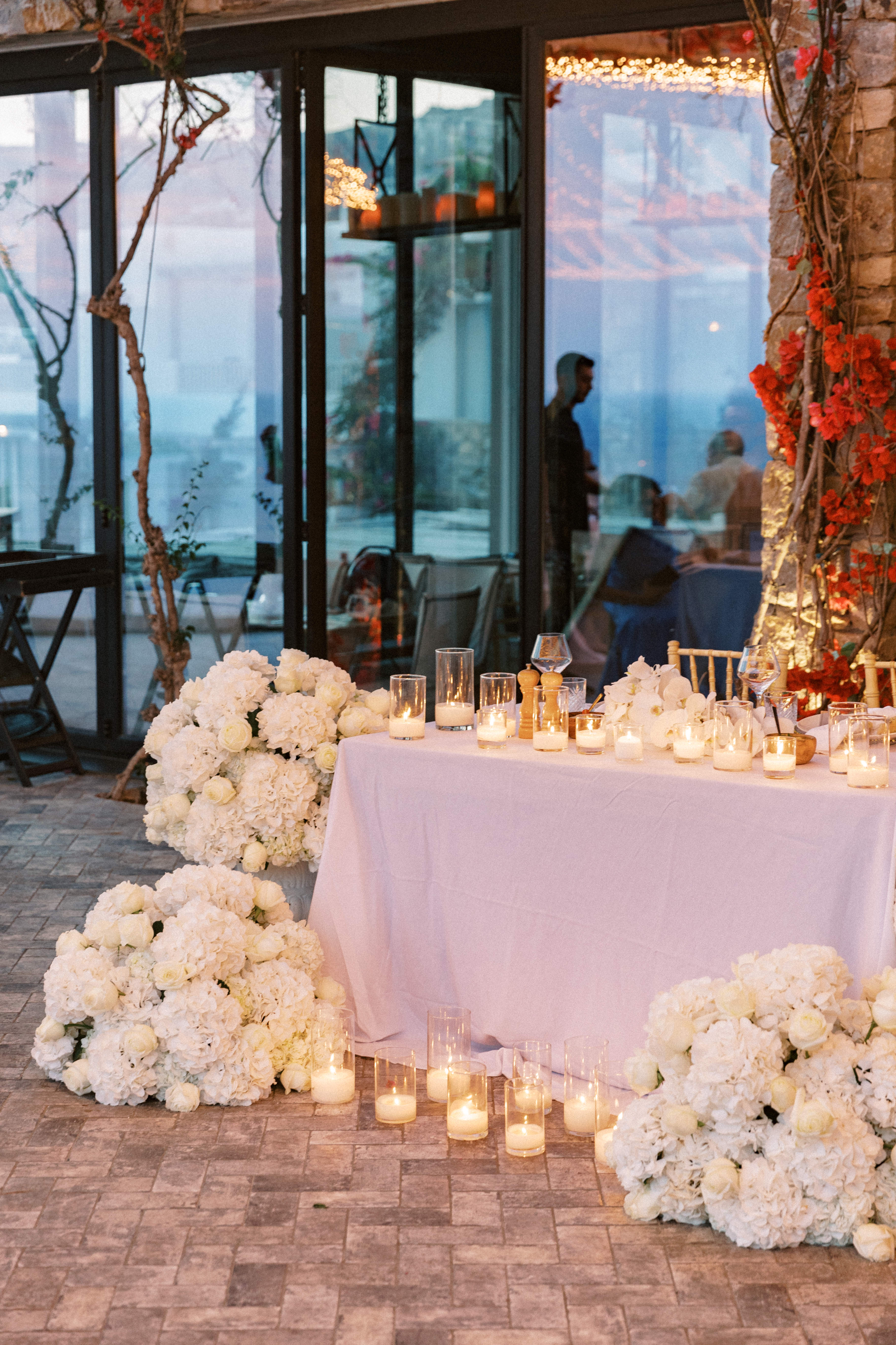 Outdoor wedding decoration under vine canopy with white flower bouquets and lit candles